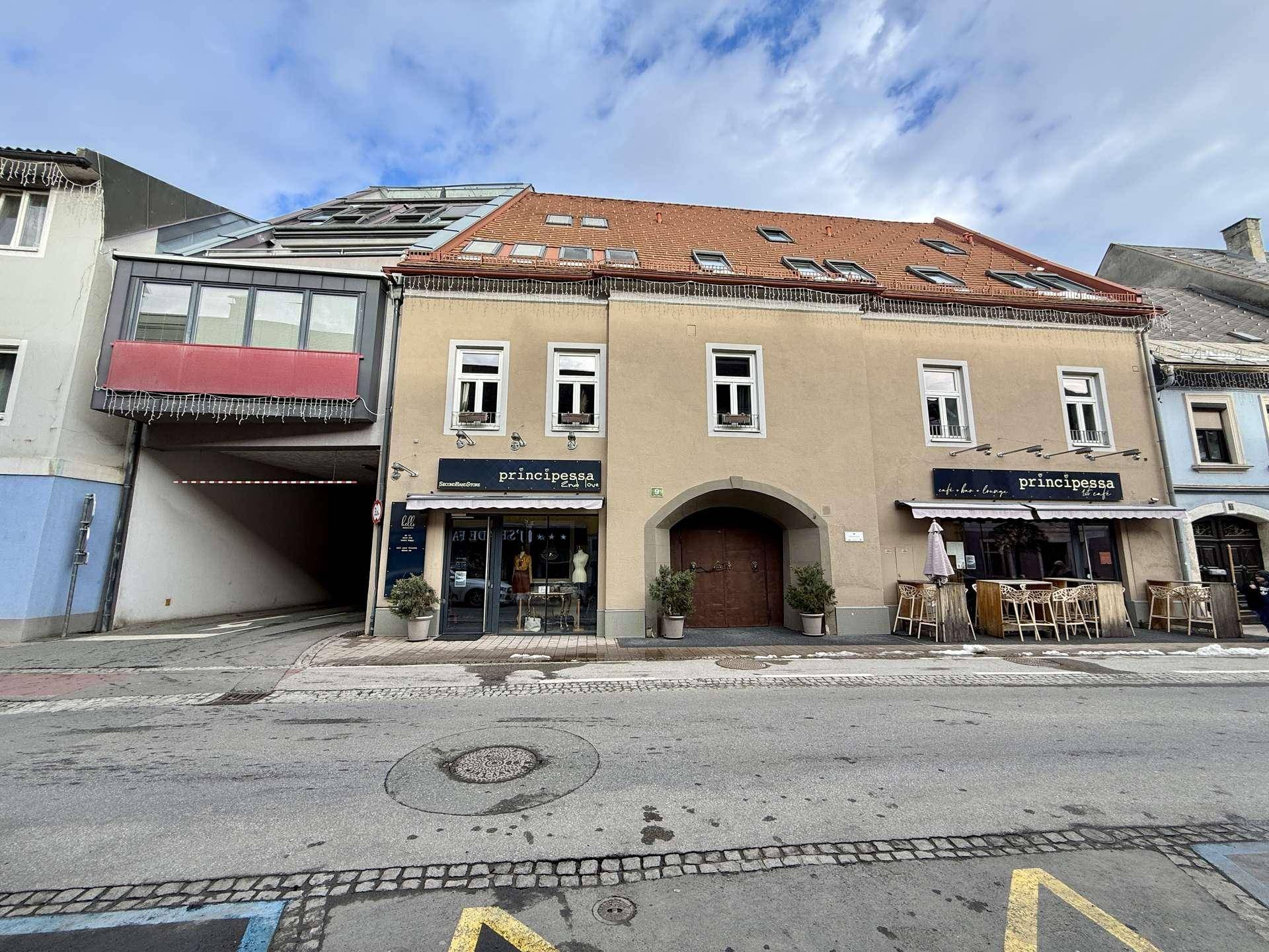 Historisches Gebäude mit Geschäften im Erdgeschoss und Wohnungen darüber an einer Straße.