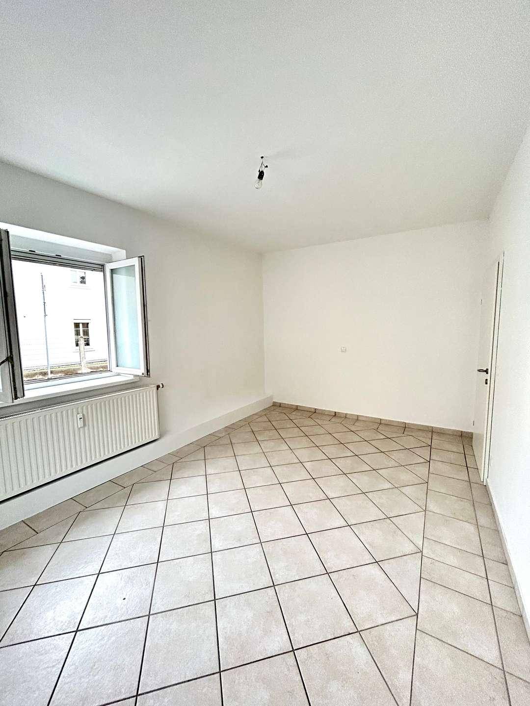 Geräumiger, leerer Raum mit Fliesenboden und einem Fenster, das Tageslicht hereinlässt.