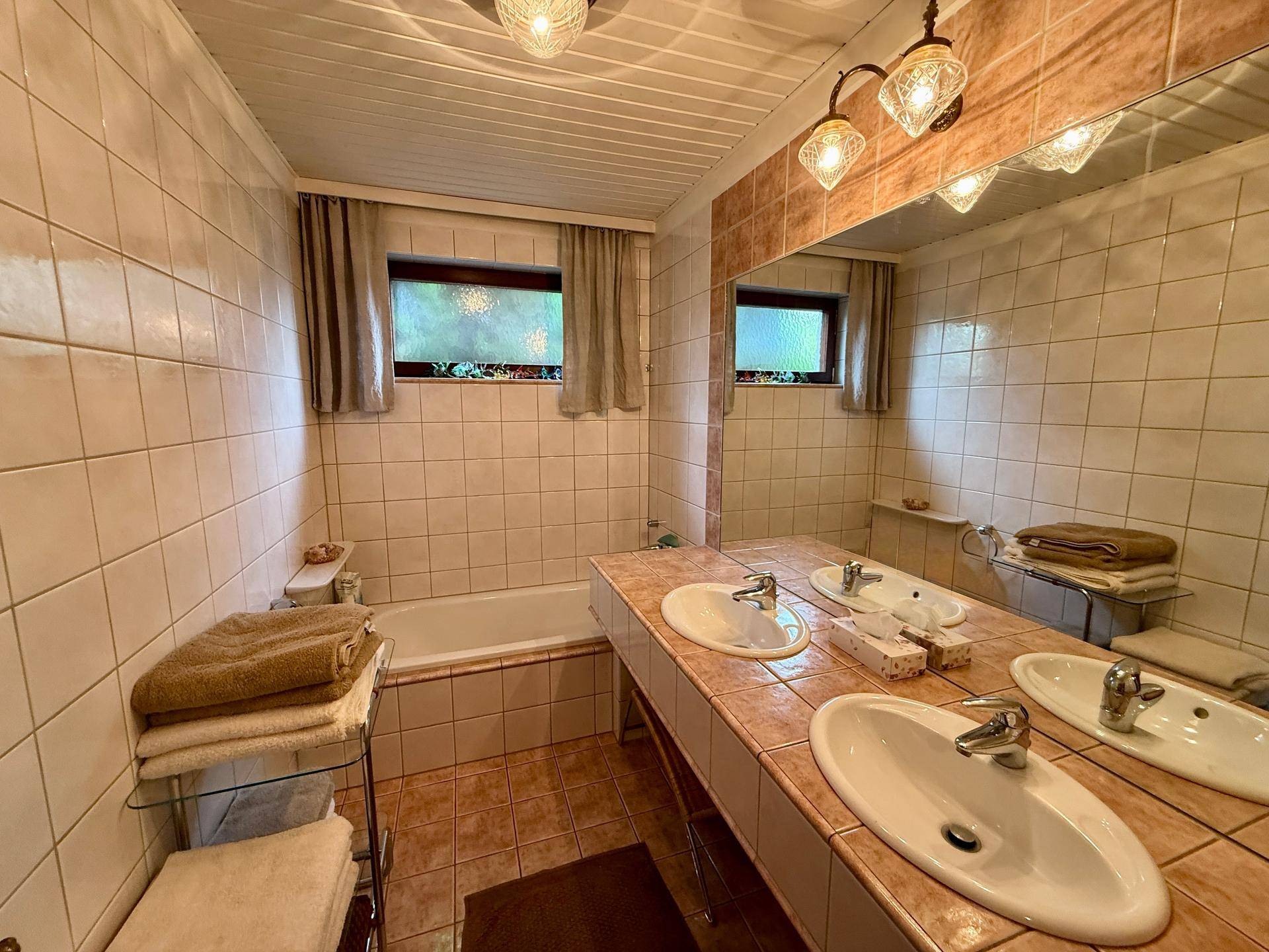 Traditionelles Badezimmer mit Doppelwaschbecken, Badewanne und beigefarbenen Fliesen.