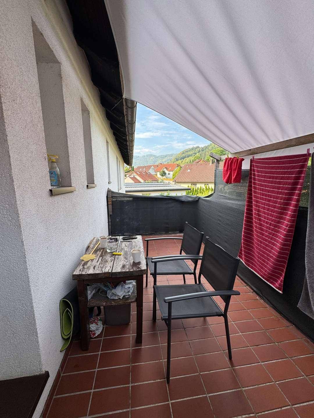 Möblierter Balkon mit Terrakottafliesen, Markise und weitem Blick ins Grüne.