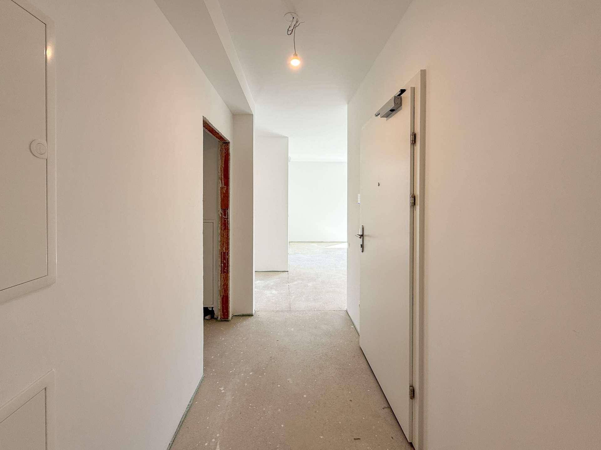Heller Flur im Rohbau mit Eingangstür und Blick in weitere unfertige Räume.