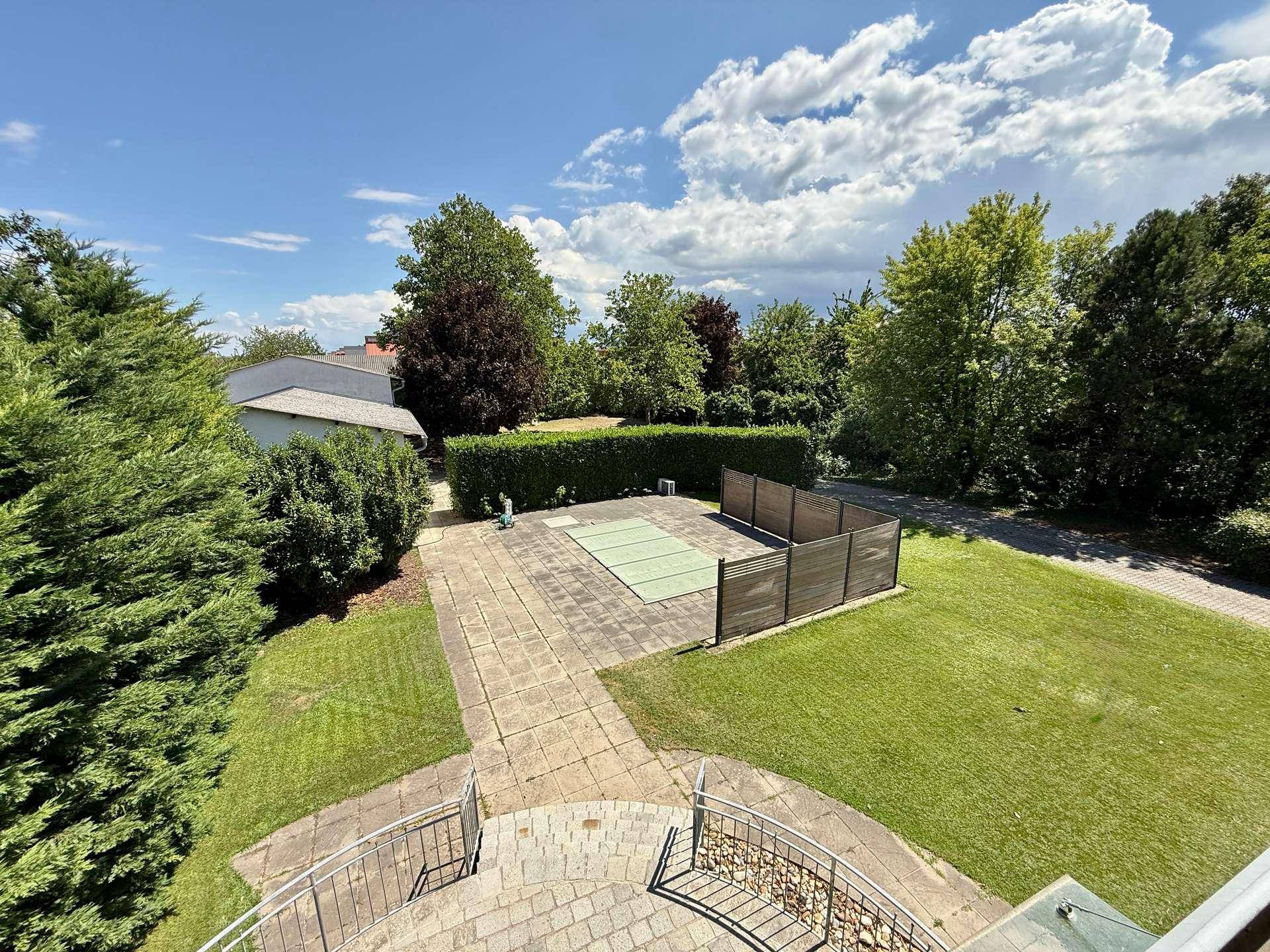 Weitläufiger Gartenbereich mit Rasenfläche, Pool und umgebenden Bäumen.