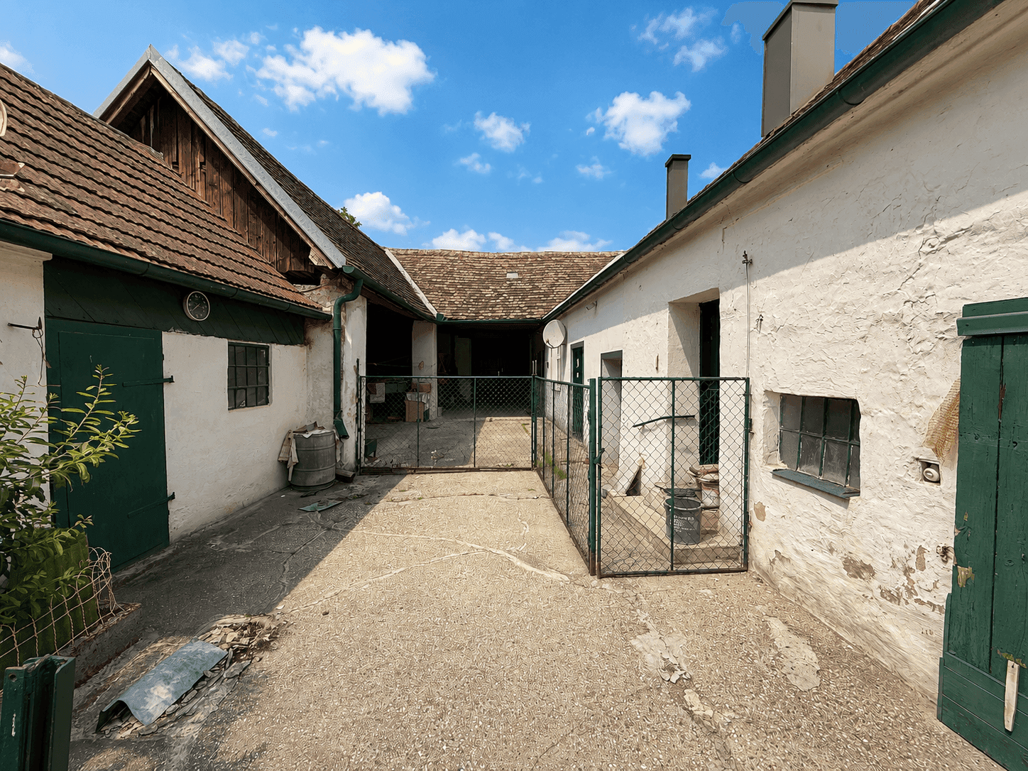 Alter Hof mit weiß getünchten Gebäuden und grünen Holztüren unter blauem Himmel.