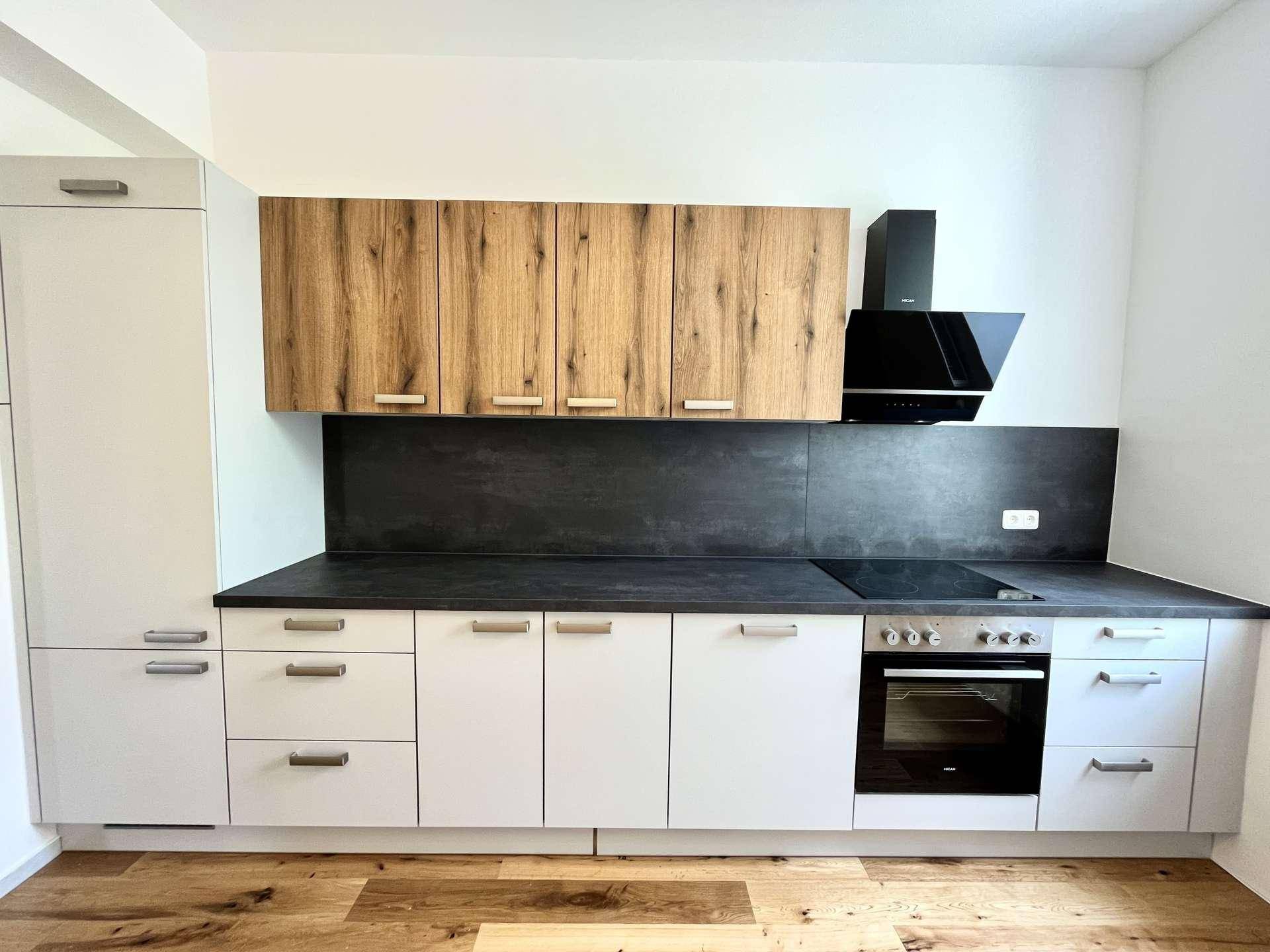 Nahaufnahme einer modernen Einbauküche mit hellen Unterschränken, Holz-Oberschränken und dunkler Arbeitsplatte.