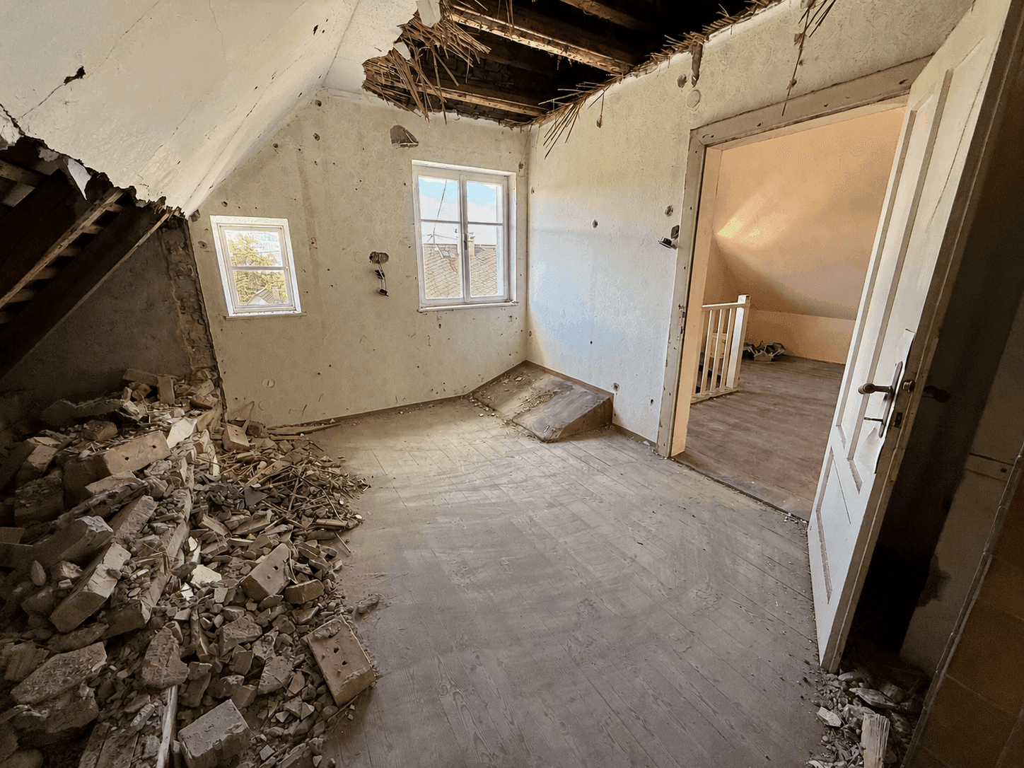 Dachgeschosszimmer im Rohzustand mit Schutt, Holzboden und Blick auf den Treppenaufgang.