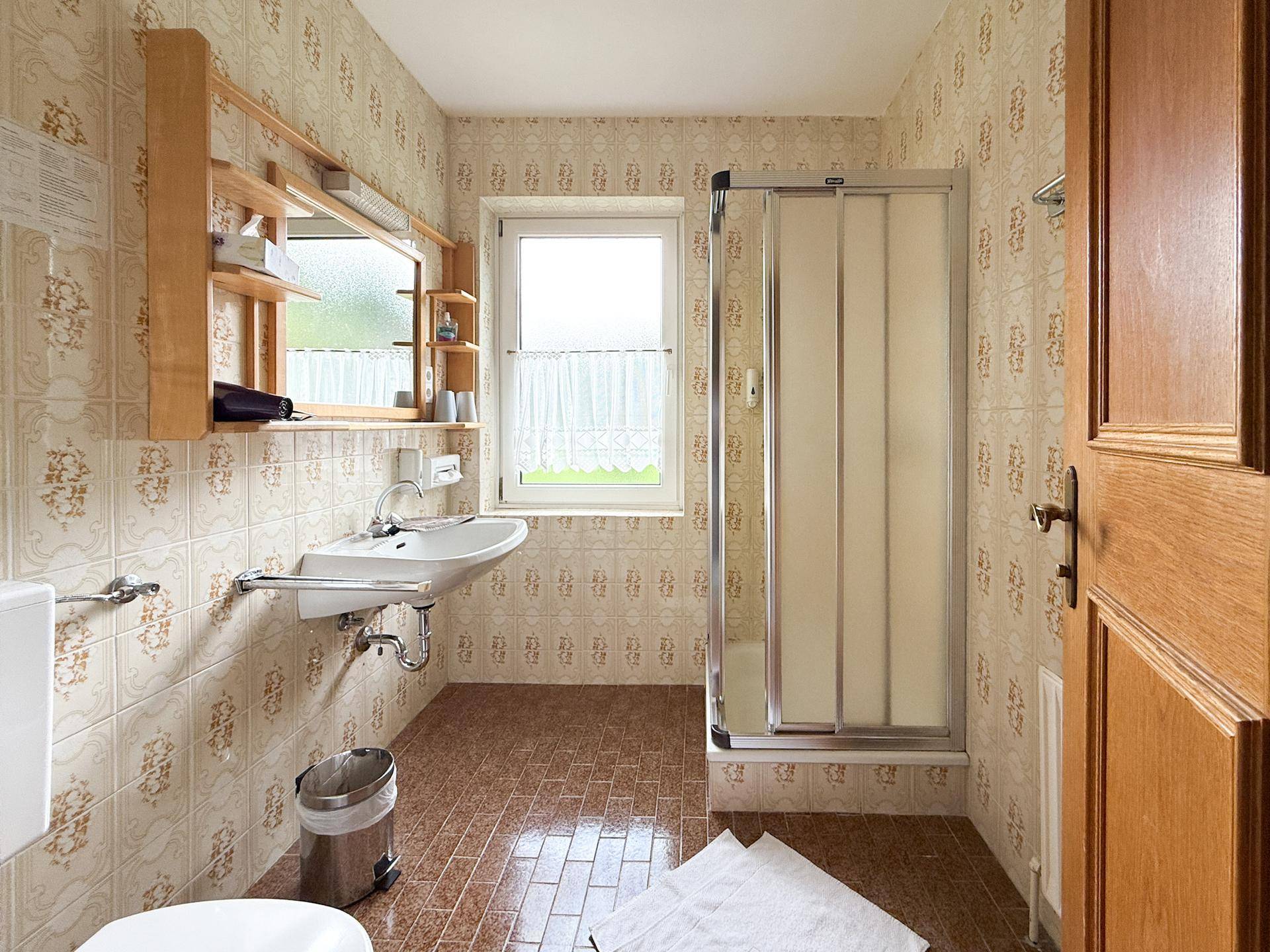 Helles Badezimmer im traditionellen Stil mit Duschkabine, Fenster und gemusterten Fliesen.