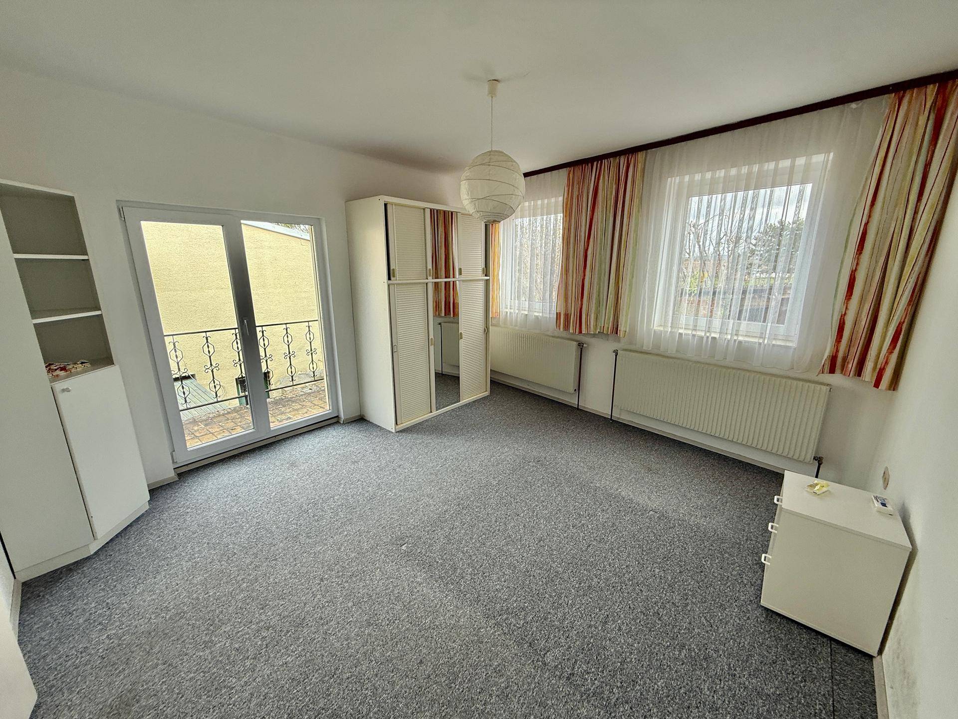 Schlafzimmer mit Teppichboden, Zugang zu einem Balkon und zwei Fenstern.