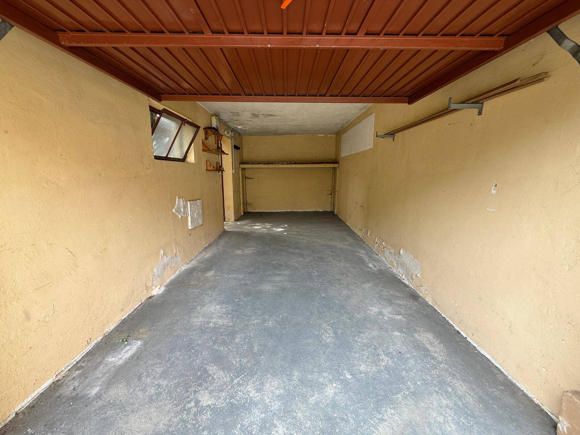 Leere Garage mit Betonboden und gelben Wänden, bietet Platz für ein Fahrzeug.