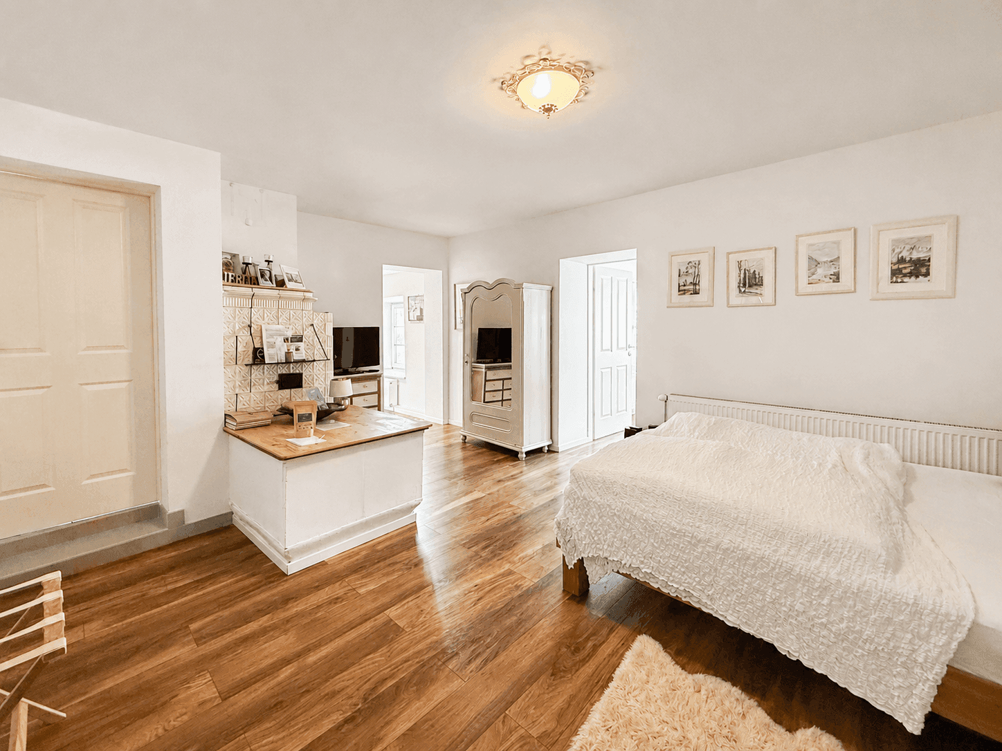 Geräumiges Schlafzimmer mit Holzboden, weißem Bett und traditionellem Kachelofen.