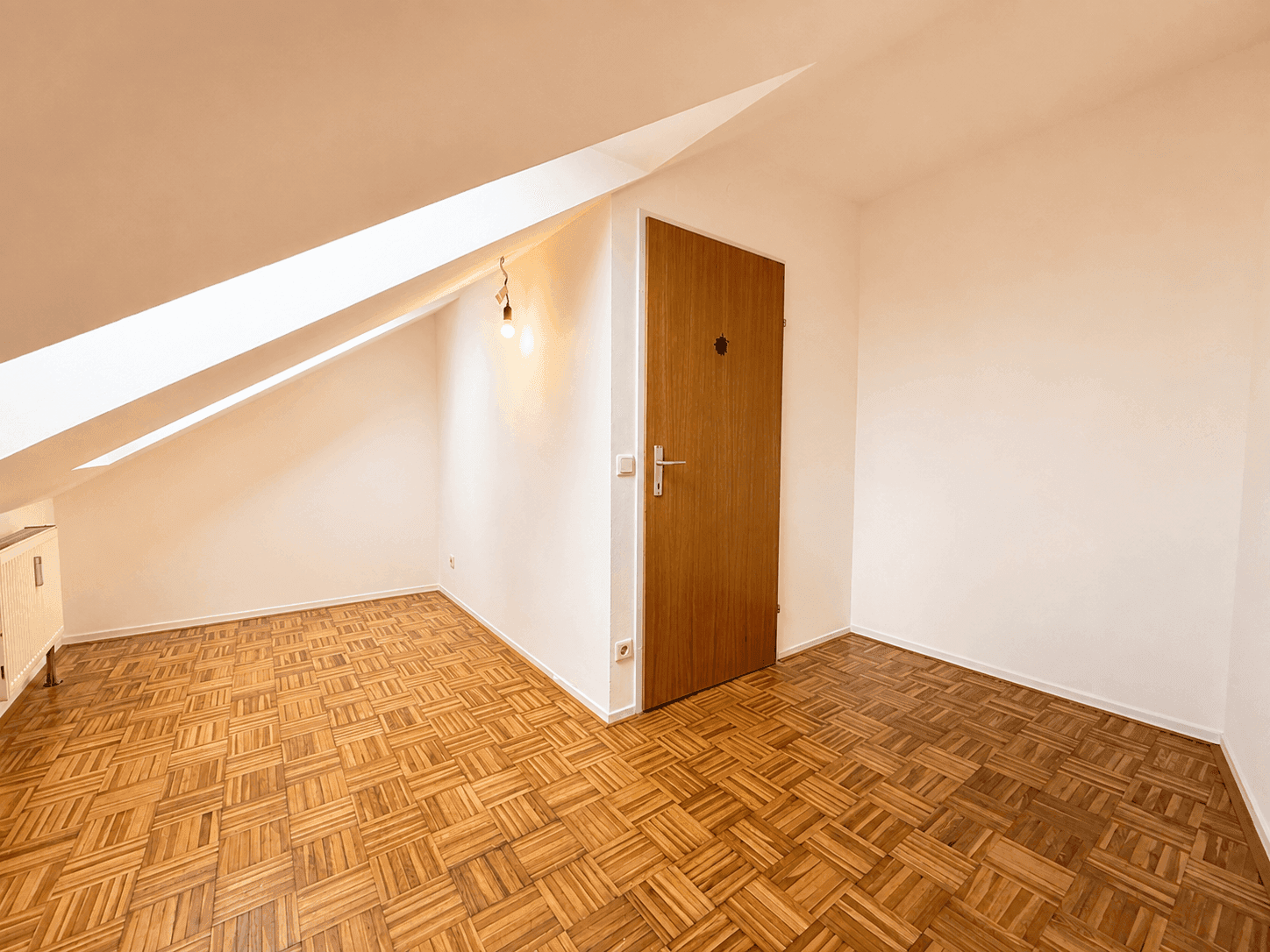 Dachgeschossraum mit Parkettboden, Dachschräge und Holztür, ideal als Schlaf- oder Arbeitszimmer.