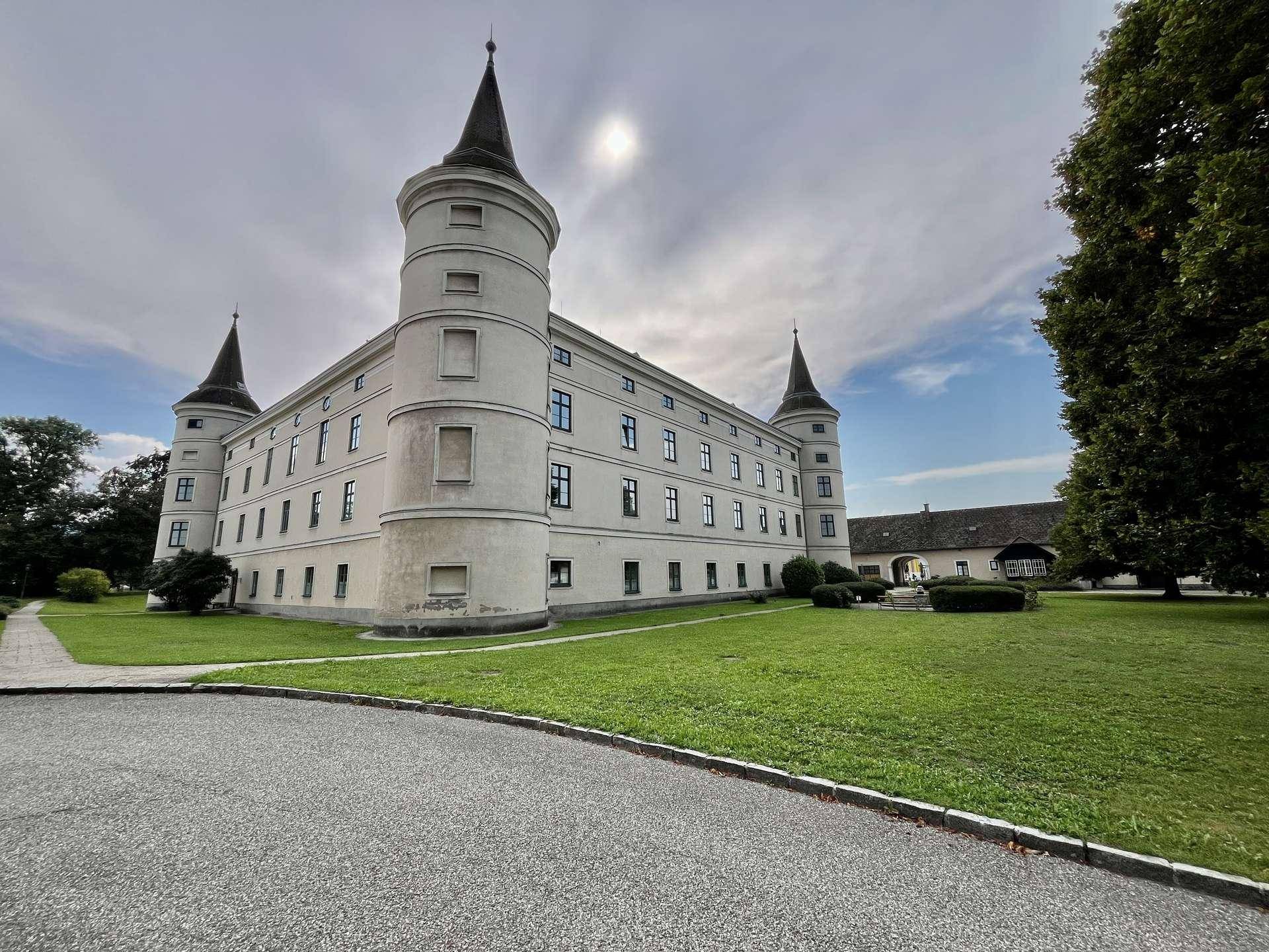 Historisches Schlossgebäude mit Türmen und gepflegter Rasenfläche unter bewölktem Himmel.