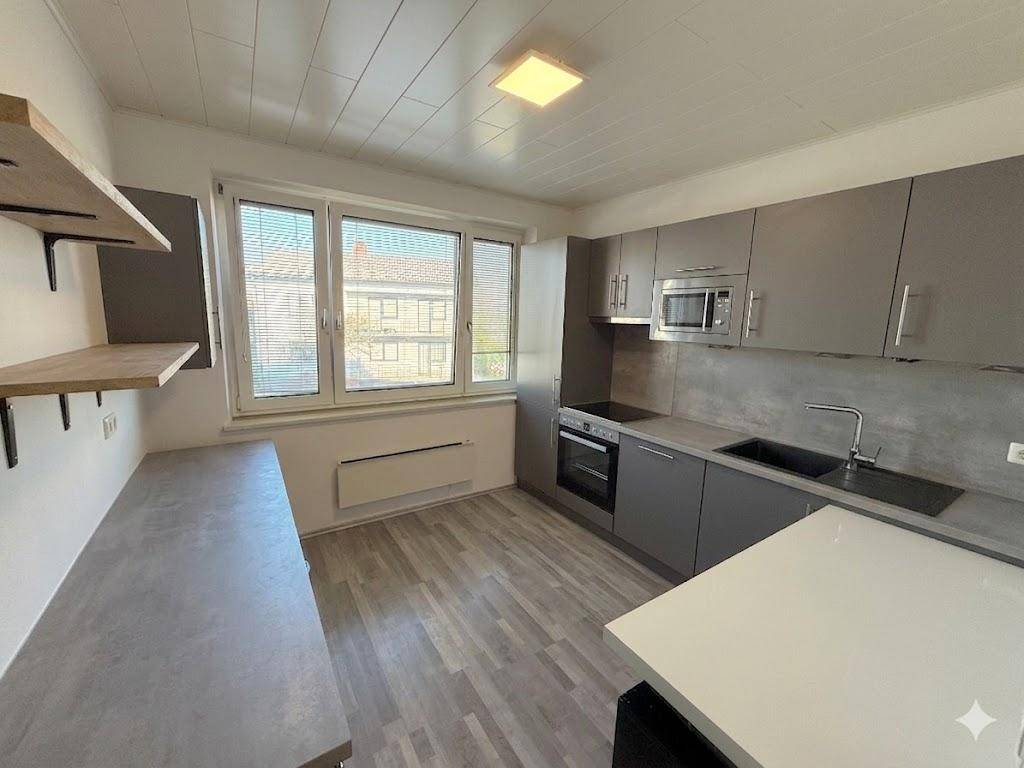 Moderne Küche mit grauen Schränken, integrierten Geräten und einem Fenster mit Blick nach draußen.