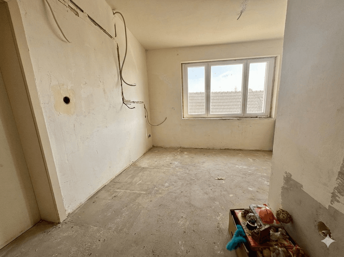 Raum im Rohbauzustand mit sichtbaren Leitungen und einem Fenster.