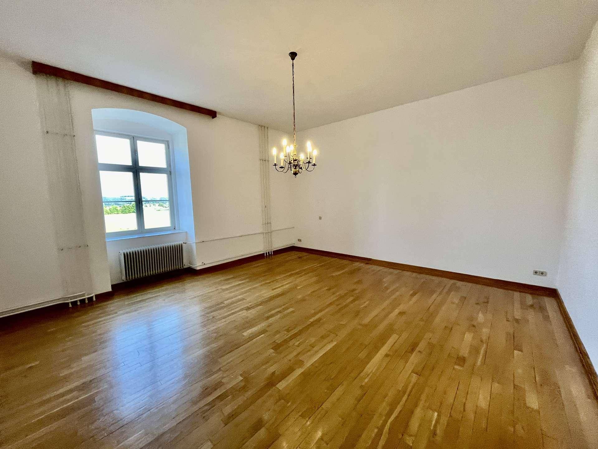 Heller Raum mit Holzboden, einem Fenster und einem eleganten Kronleuchter an der Decke.