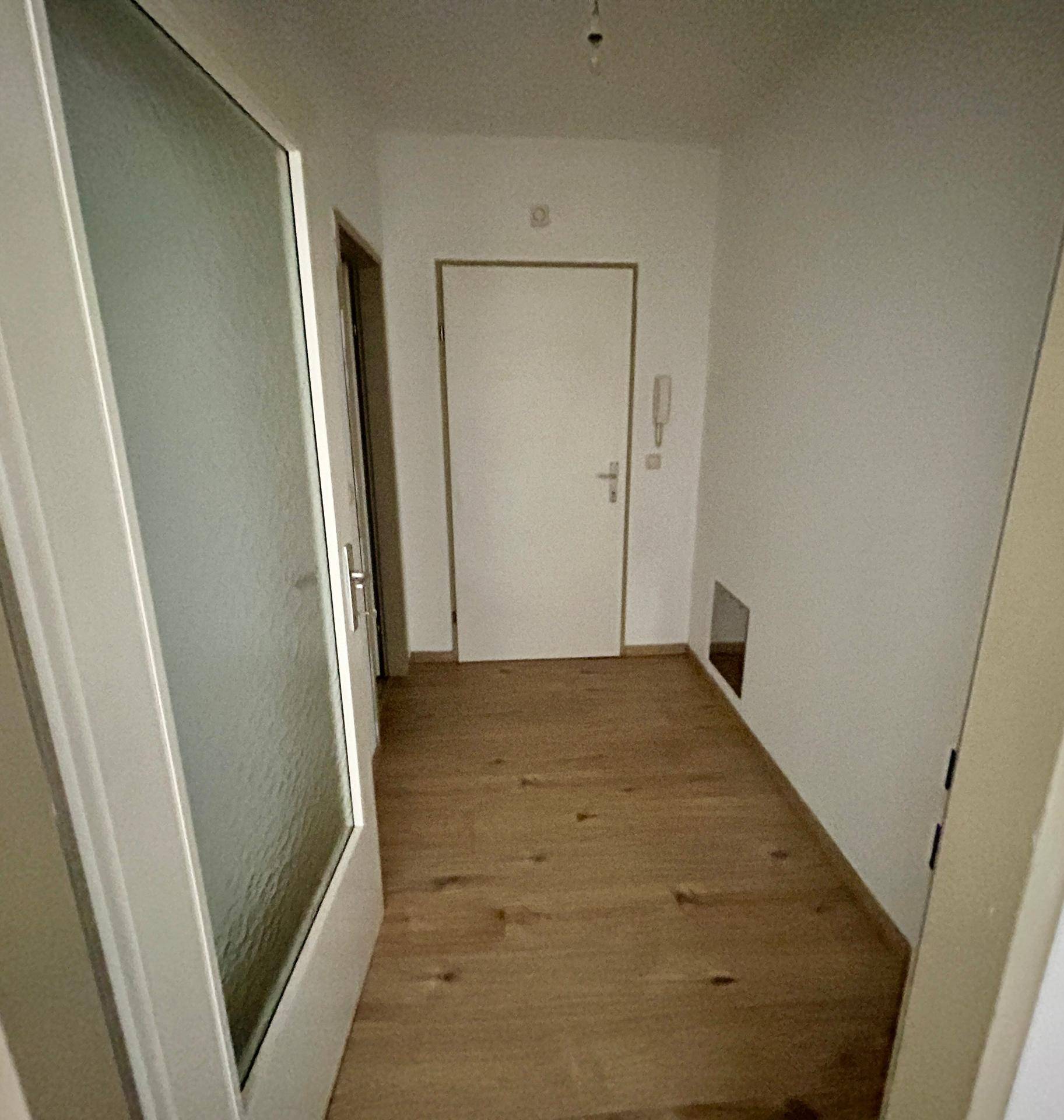 Heller Flur mit Laminatboden und mehreren Türen, darunter eine mit Milchglas, die zu weiteren Räumen führt.
