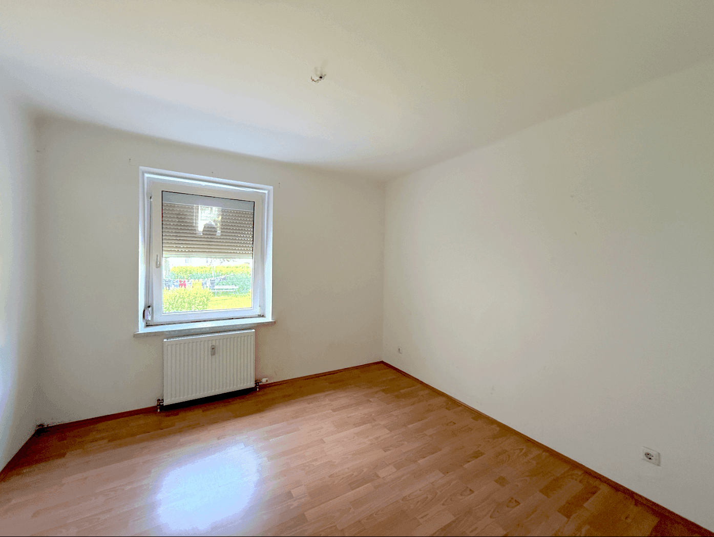 Unmöbliertes Schlafzimmer mit Laminatboden, weiß gestrichenen Wänden und einem Fenster mit Rollladen.