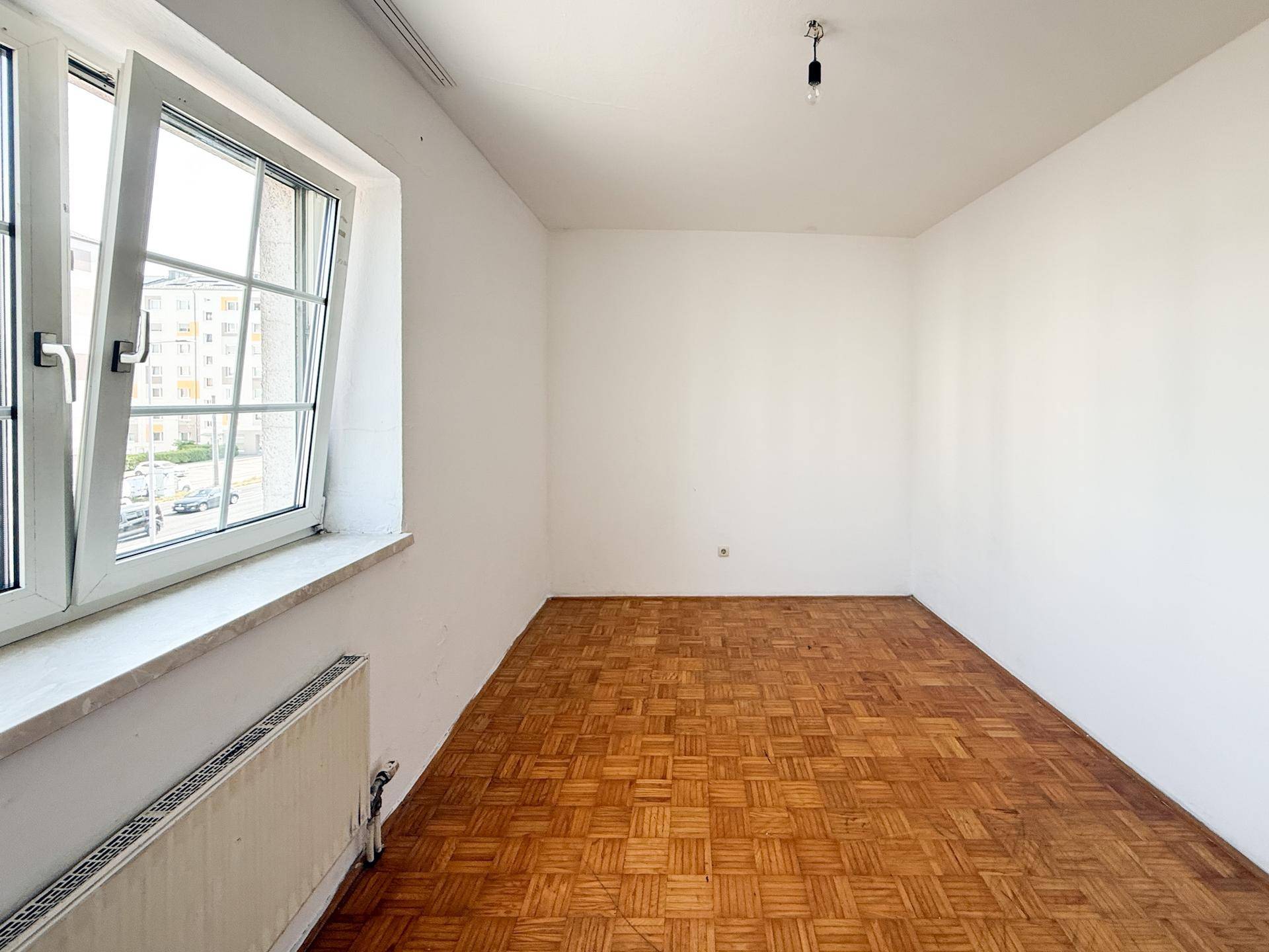 Helles Zimmer mit geöffnetem Fenster und Parkettboden, ideal für frische Luft und Tageslicht.