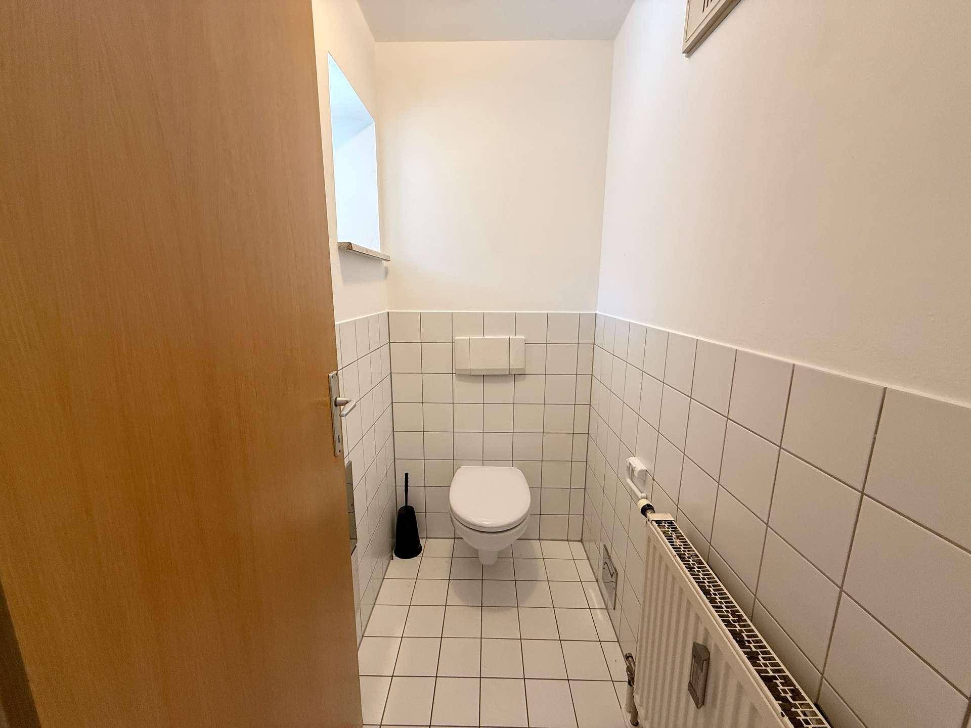 Kleines WC mit weißen Fliesen, Toilette und Heizkörper, ideal als Gästetoilette.