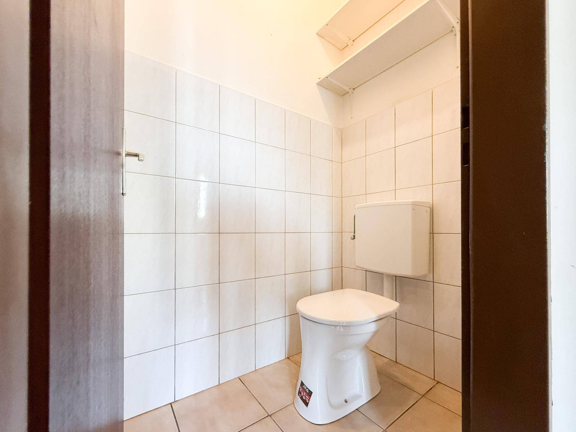 Separates WC mit weißen Fliesen und einfacher Toilette, funktional und sauber.