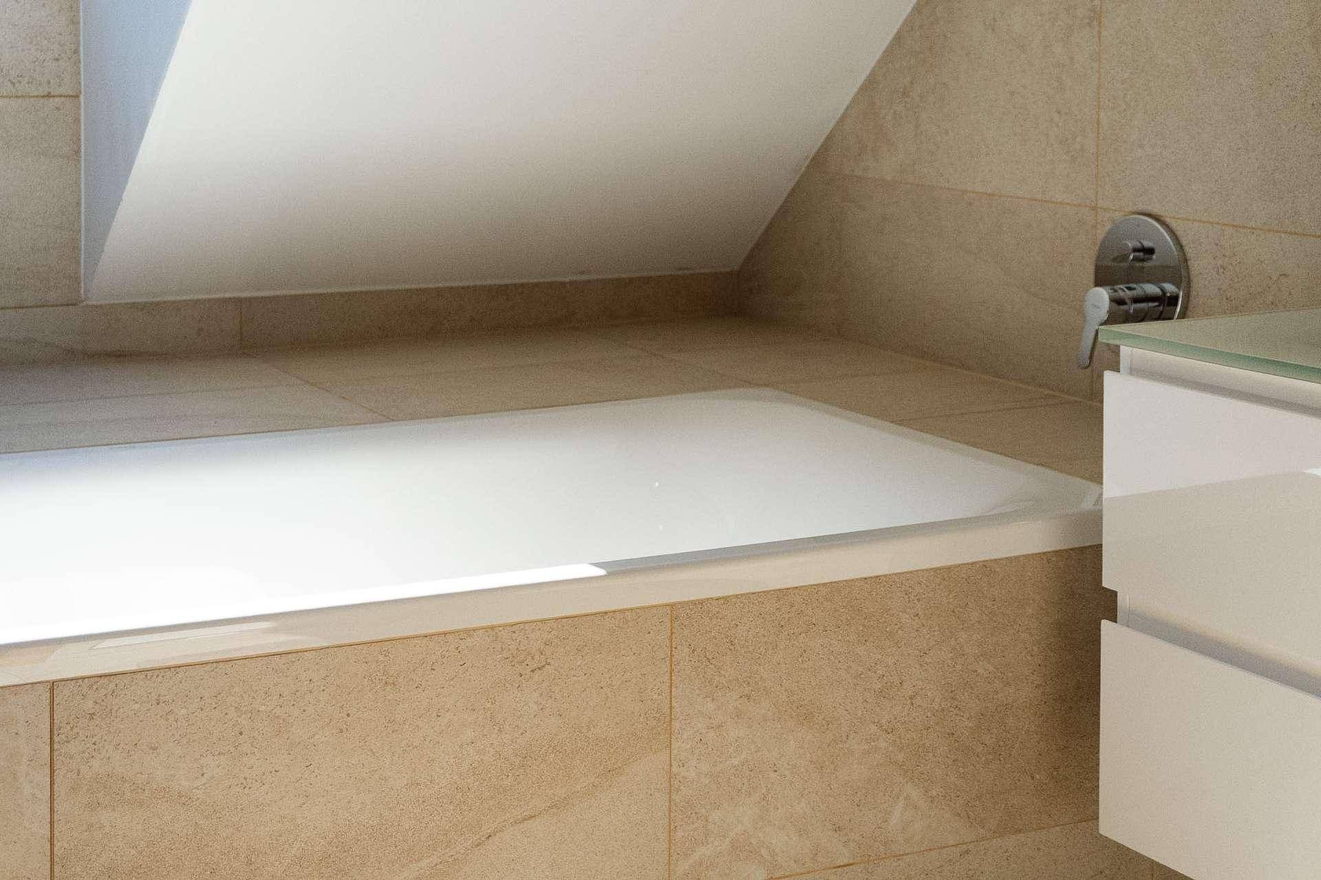 Detailansicht der eingebauten Badewanne und des Waschtischs in einem modern gefliesten Badezimmer.