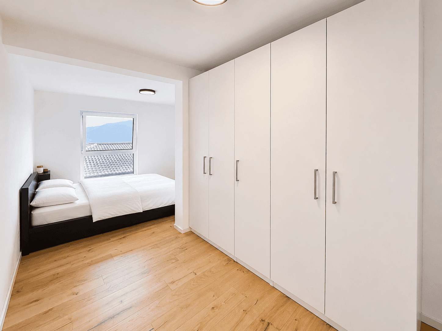 Schlafzimmer mit Einbauschränken, Holzboden und Blick auf die Dächer.