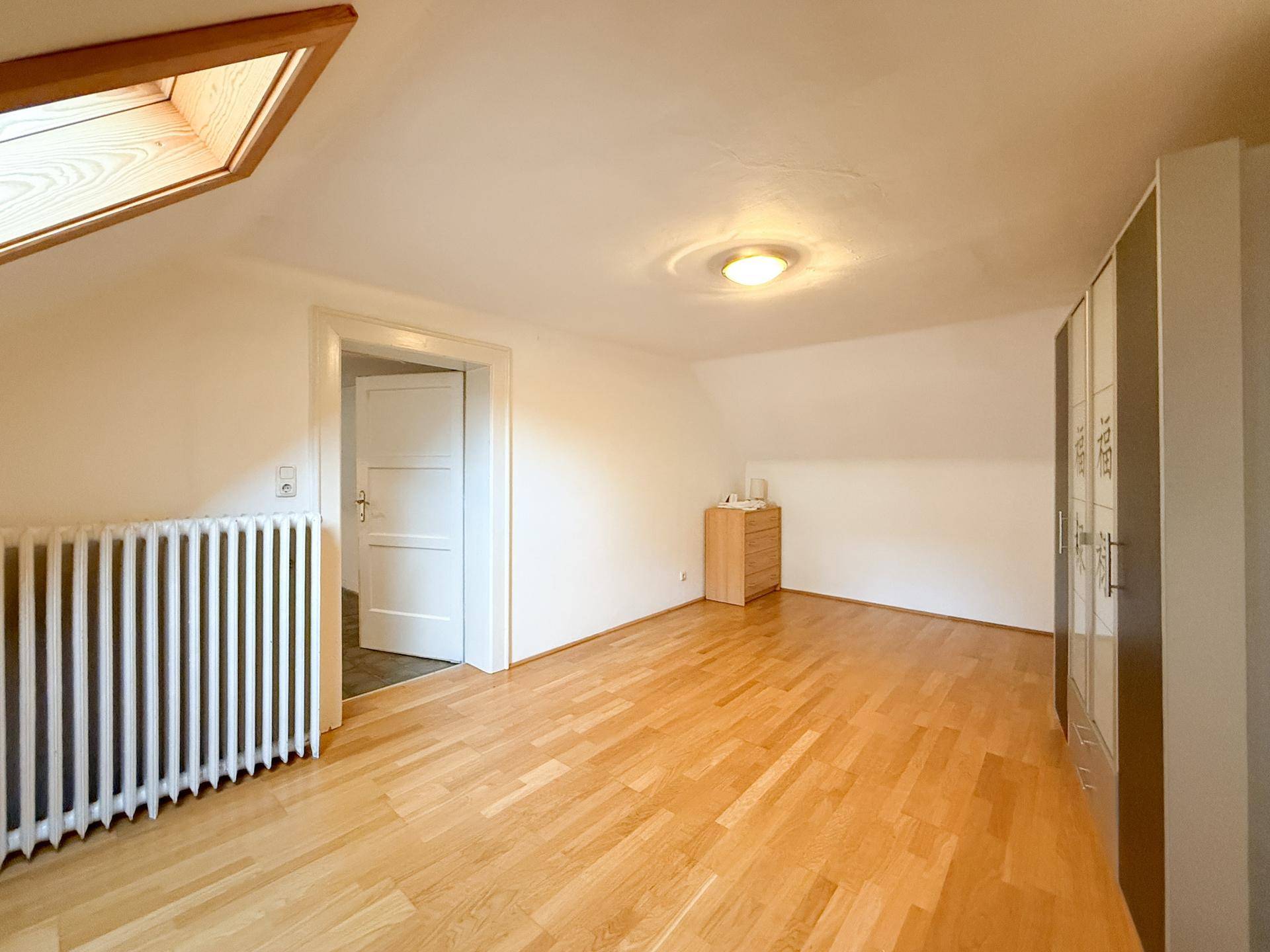 Helles Schlafzimmer im Dachgeschoss mit Holzboden, Dachfenster und Zugang zum Flur.