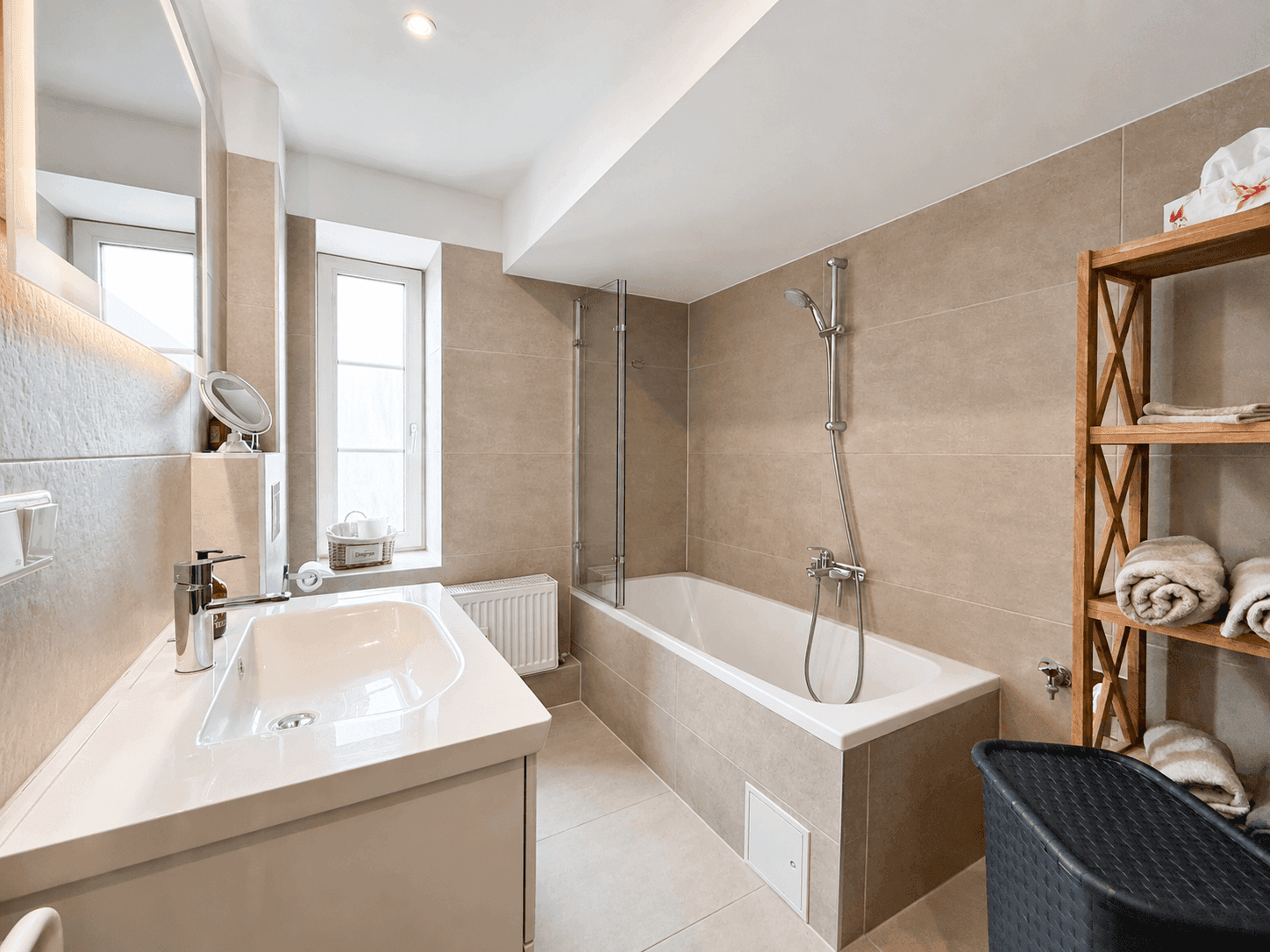 Modernes Badezimmer mit beigefarbenen Fliesen, Badewanne und Fenster für Tageslicht.