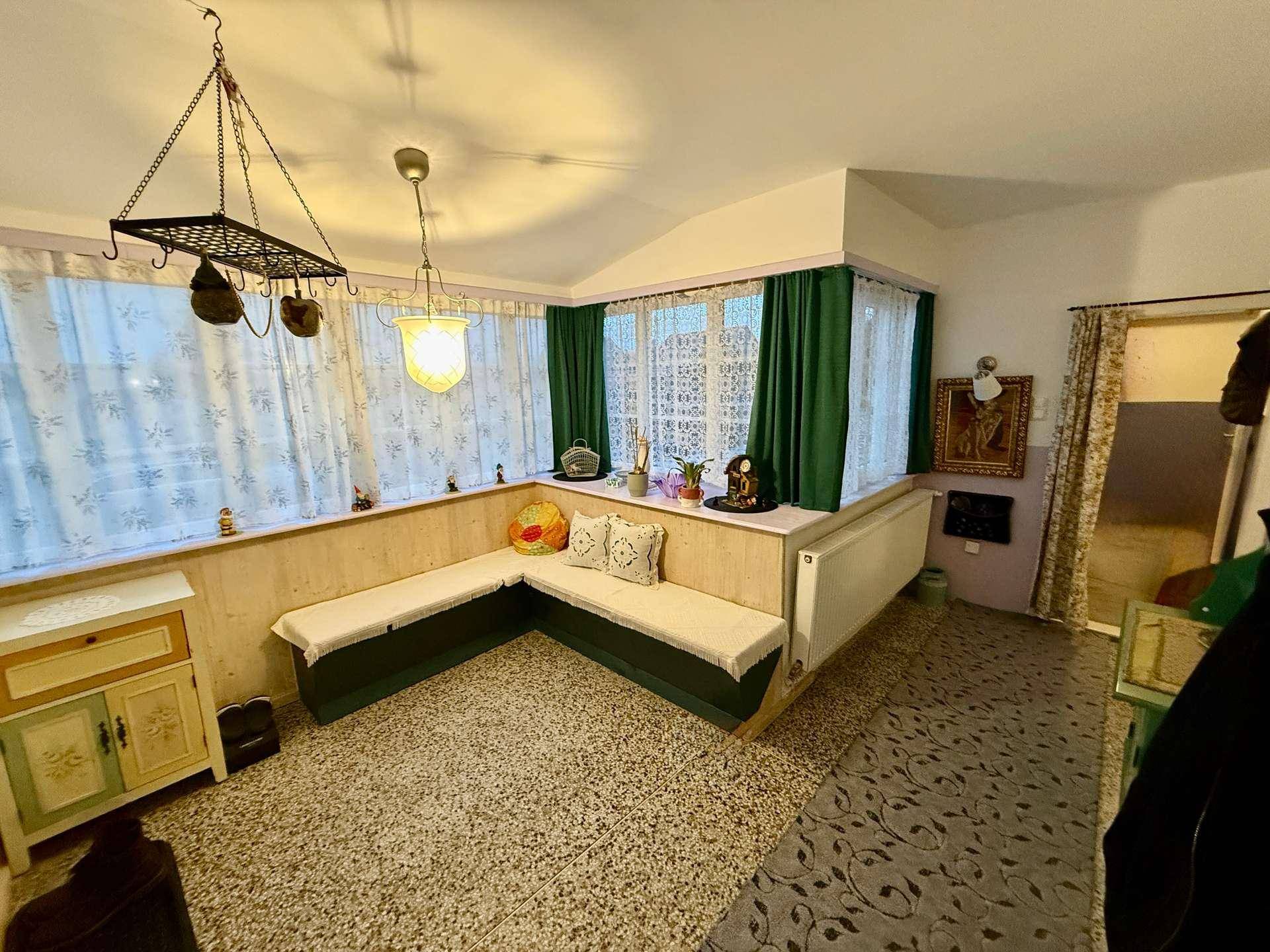 Heller Wintergarten mit integrierter Sitzbank, vielen Fenstern und einem angenehmen Blick ins Grüne.