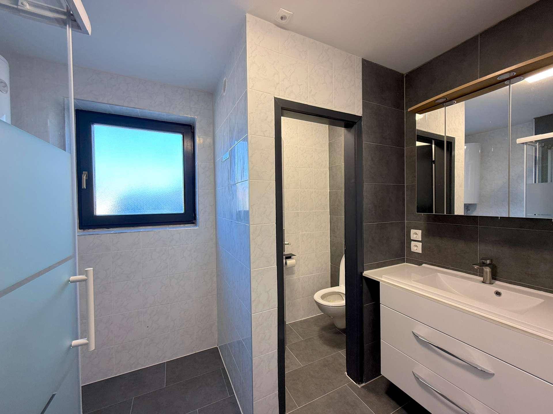 Modernes Badezimmer mit grauen und weißen Fliesen, einem Waschtisch und einer begehbaren Dusche.