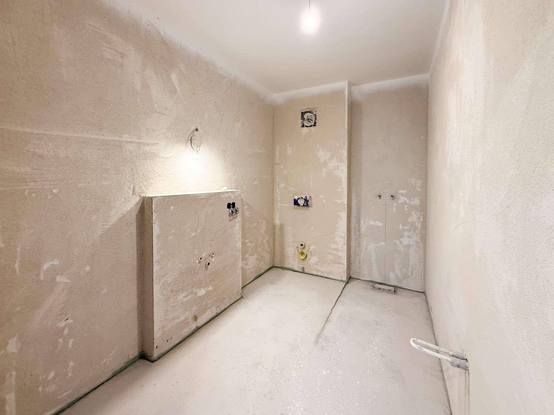 Unfertiges Badezimmer im Rohbau mit vorbereiteten Anschlüssen für Sanitärinstallationen.