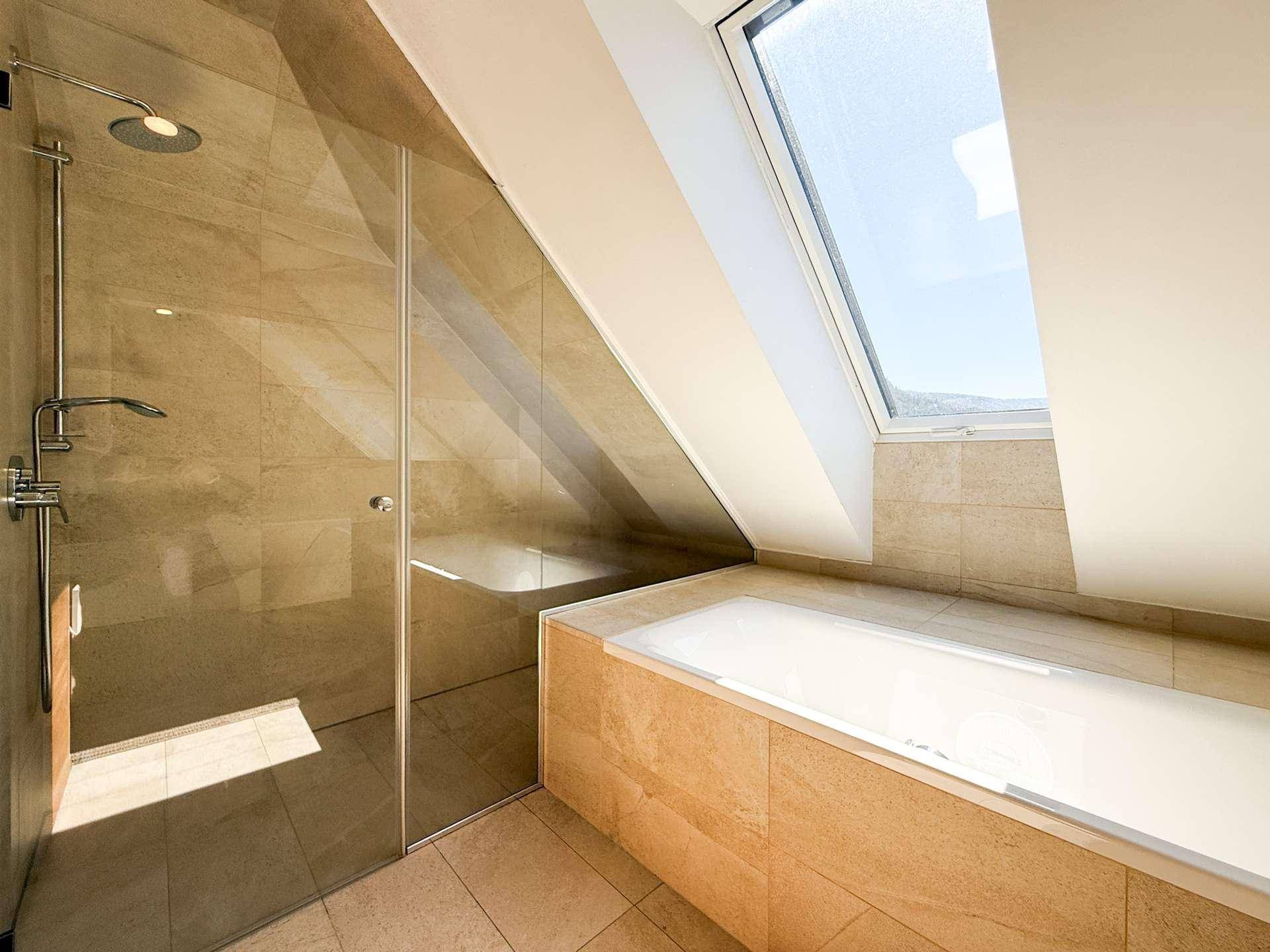 Modernes Badezimmer mit begehbarer Dusche, Badewanne und einem Dachfenster, das den Raum erhellt.