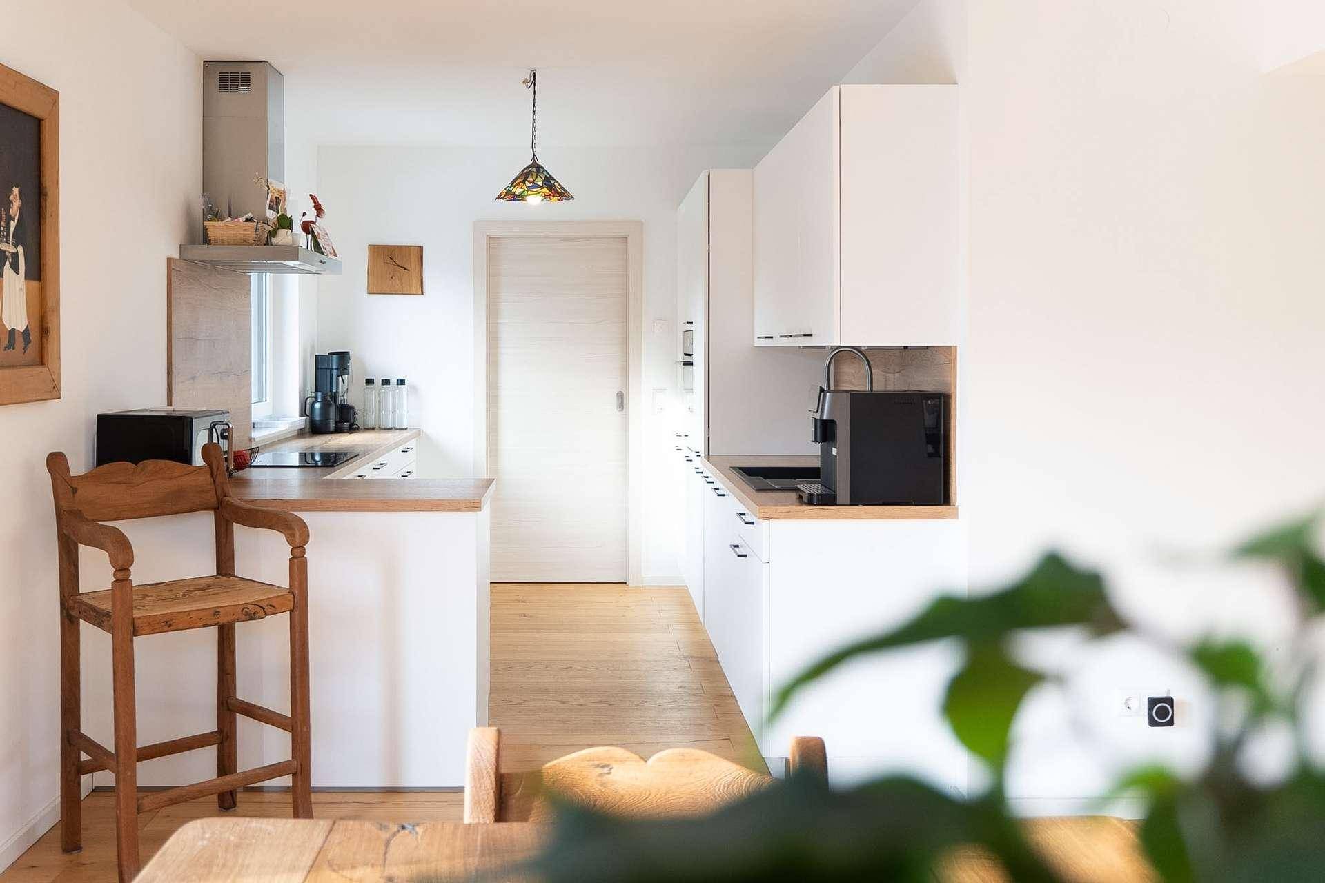 Moderne Küche mit weißen Schränken, Holztheke und integrierten Geräten.