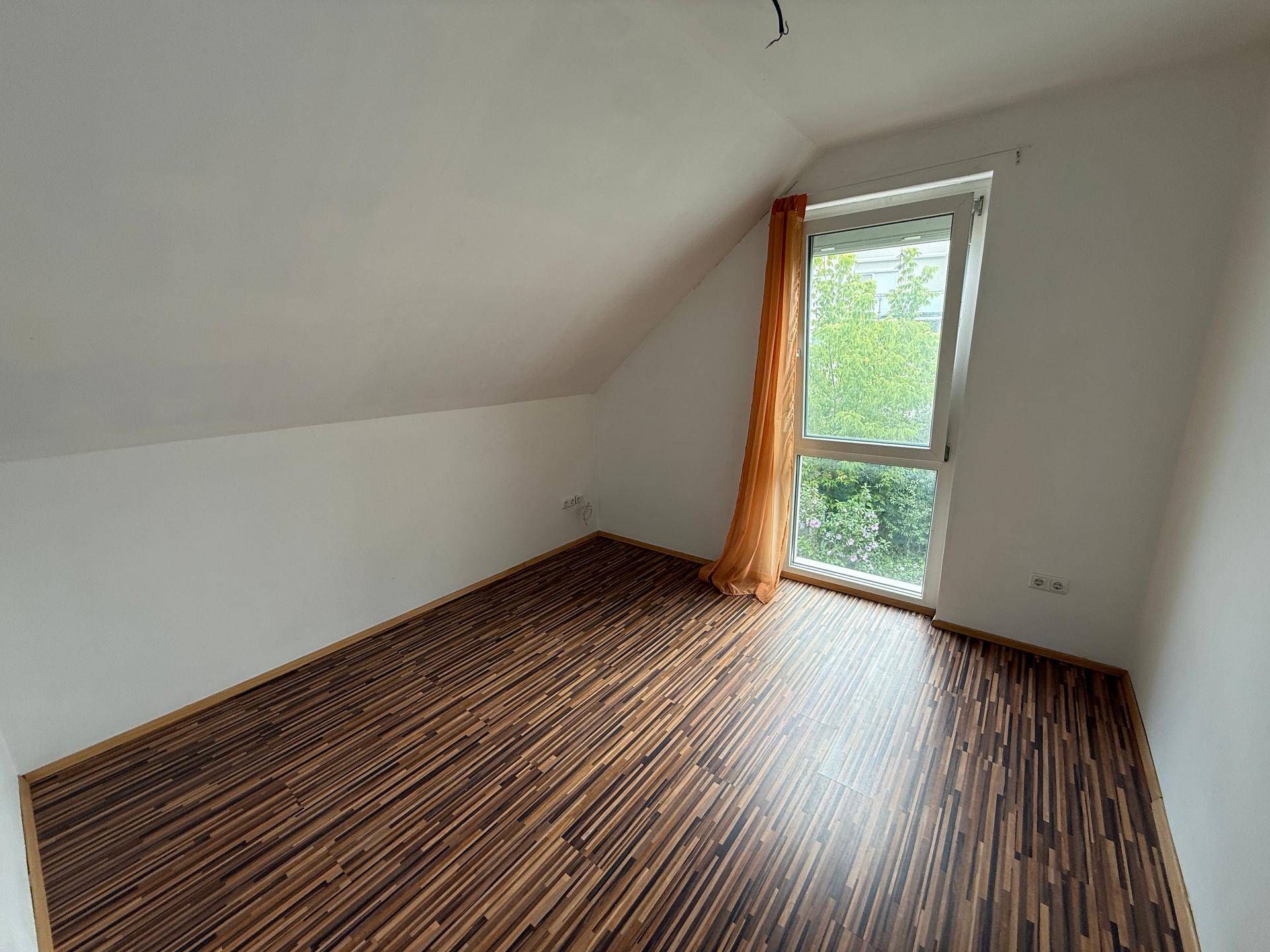 Dachgeschoss-Schlafzimmer mit Laminatboden, Dachschräge und einem großen Fenster.