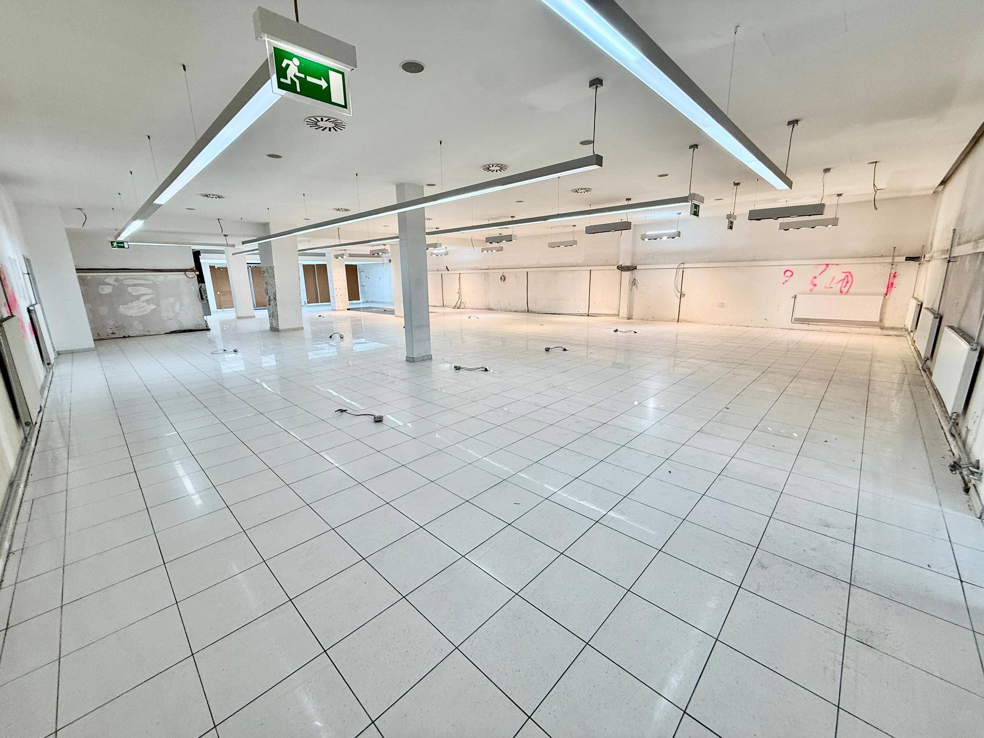 Geräumige, leere Gewerbefläche mit Fliesenboden und abgehängten Deckenleuchten, bereit für den Ausbau.