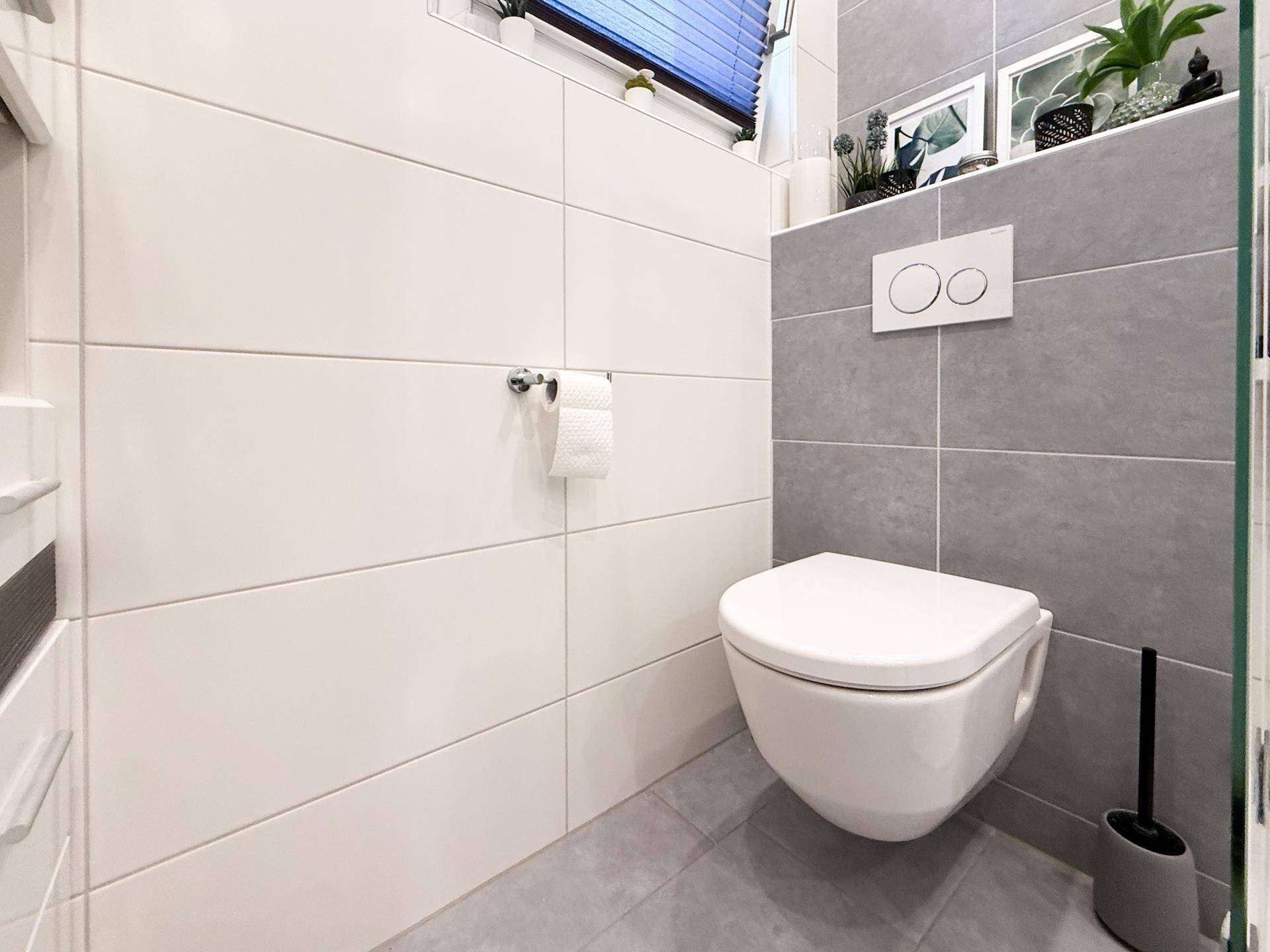 Modernes WC mit wandhängender Toilette und stilvollen Fliesen in Weiß und Grau.