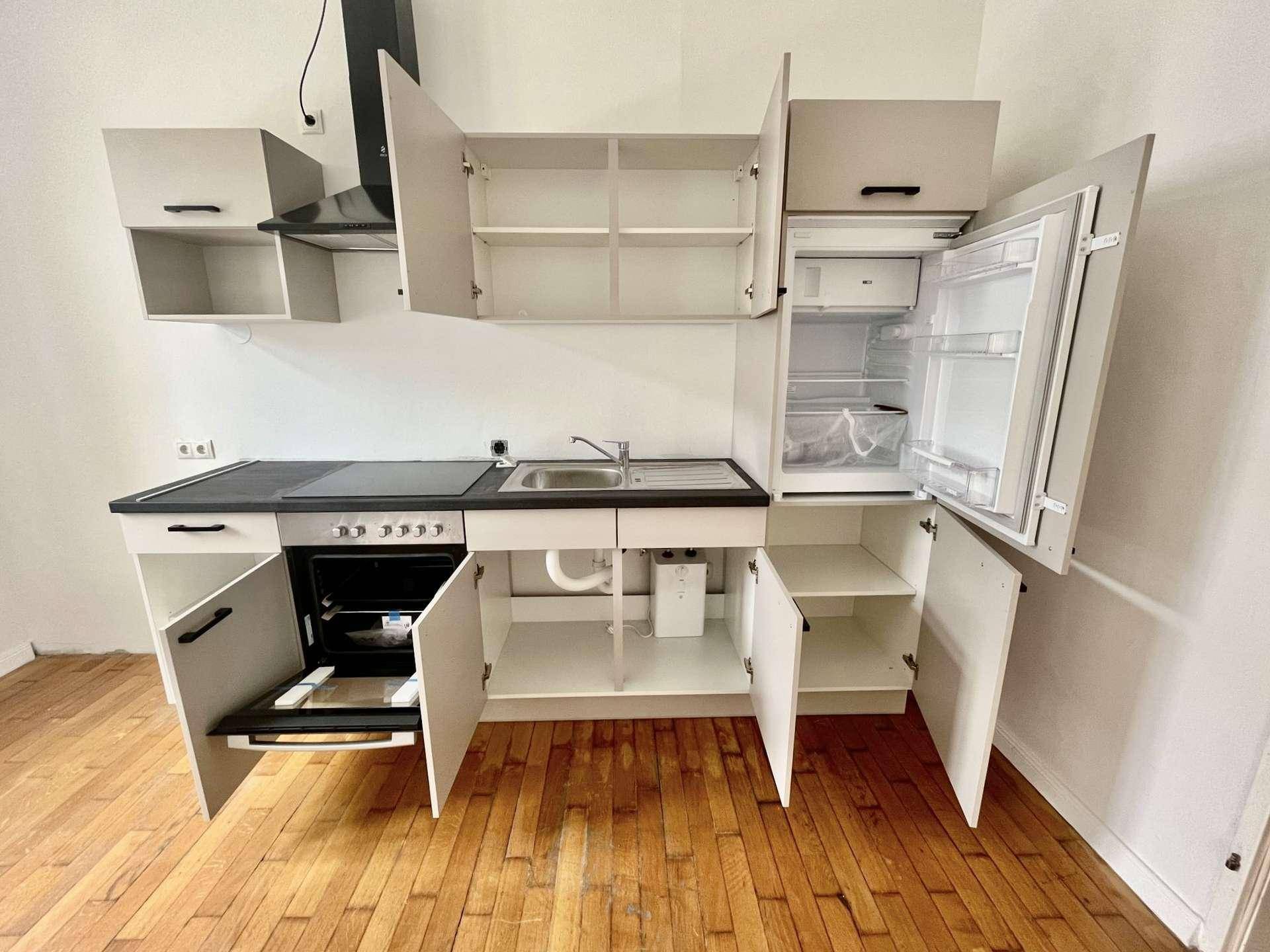 Kompakte Einbauküche mit geöffneten Schränken, integriertem Kühlschrank und Kochfeld, praktisch und platzsparend.