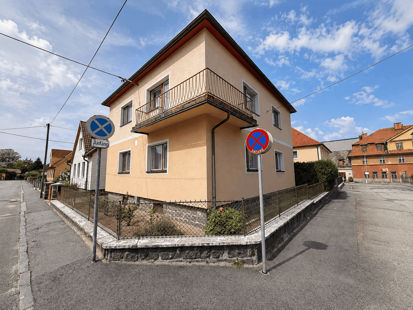 Eckansicht des Hauses an einer Straße mit Balkon und kleiner Gartenfläche.