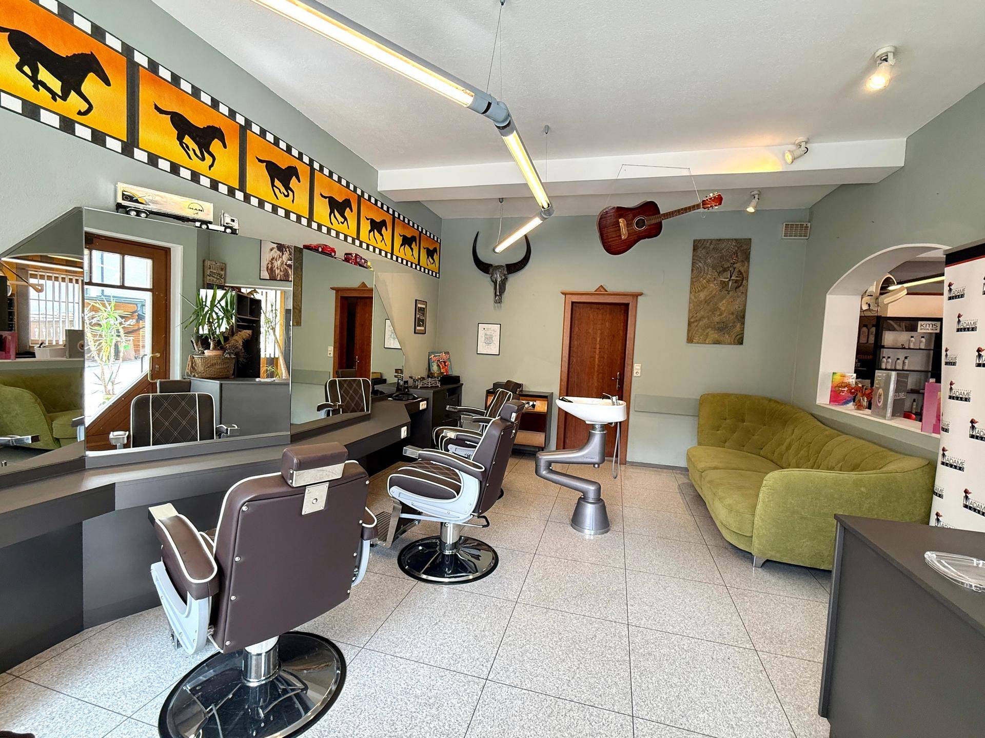 Stilvoller Friseursalon mit grüner Couch, Styling-Stühlen und dekorativen Elementen.