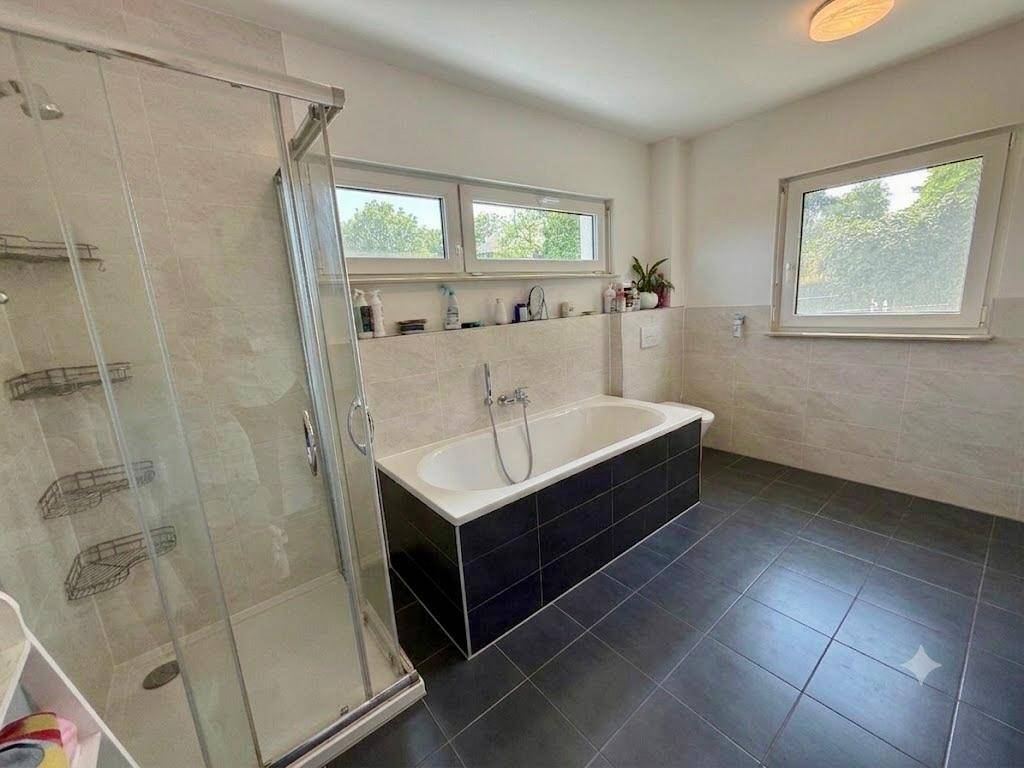 Modernes Badezimmer mit Badewanne, separater Dusche und Fenster für Tageslicht.