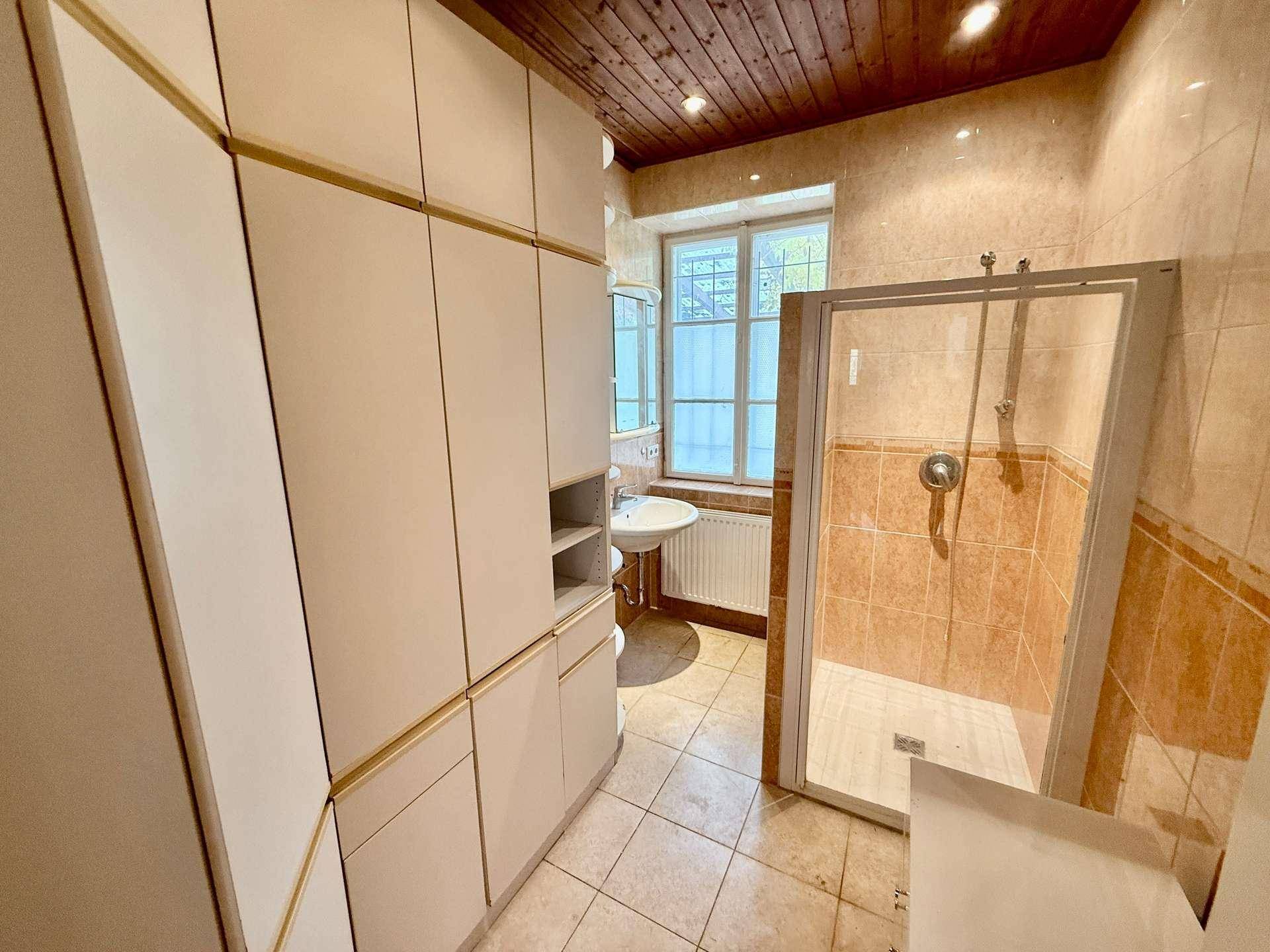 Badezimmer mit Duschkabine, Waschbecken und Einbauschränken unter Holzdecke.