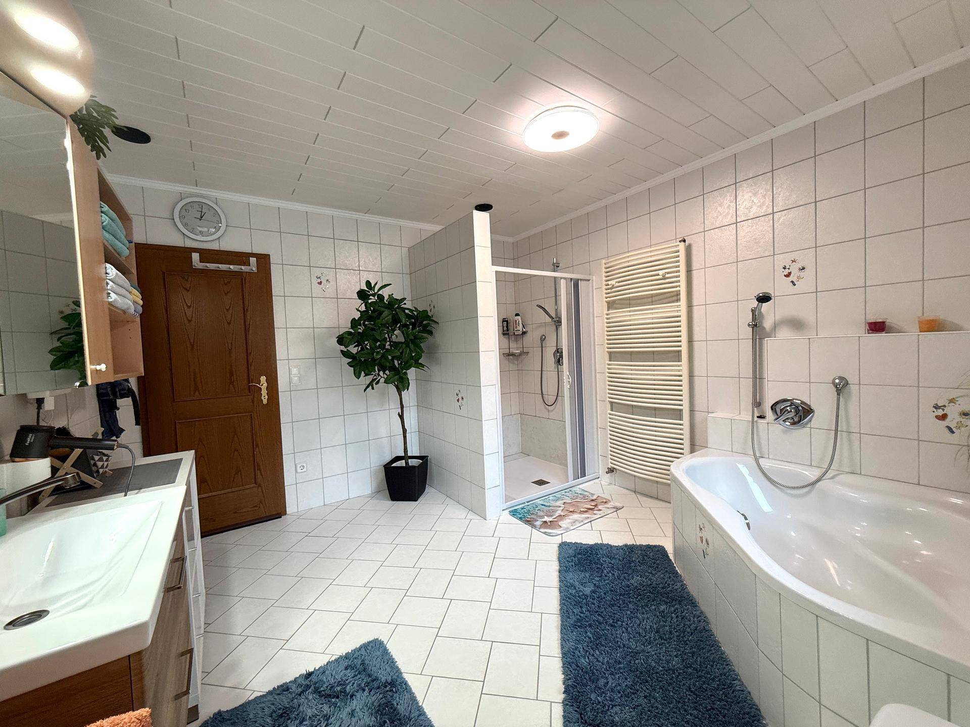 Geräumiges Badezimmer mit Badewanne, Dusche, Fliesen und beheiztem Handtuchhalter.