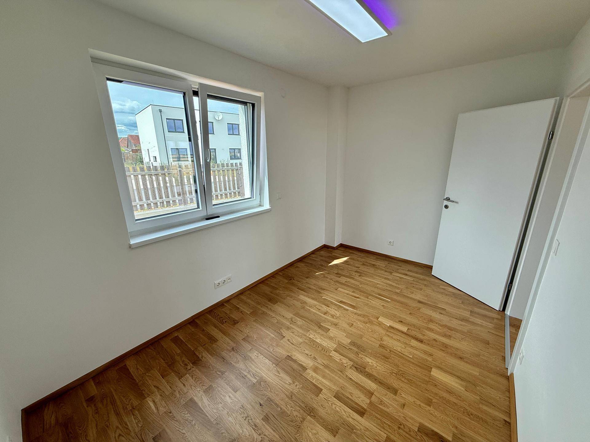 Kleines Zimmer mit Holzboden und Fenster, das einen Blick auf die Nachbarbebauung bietet.