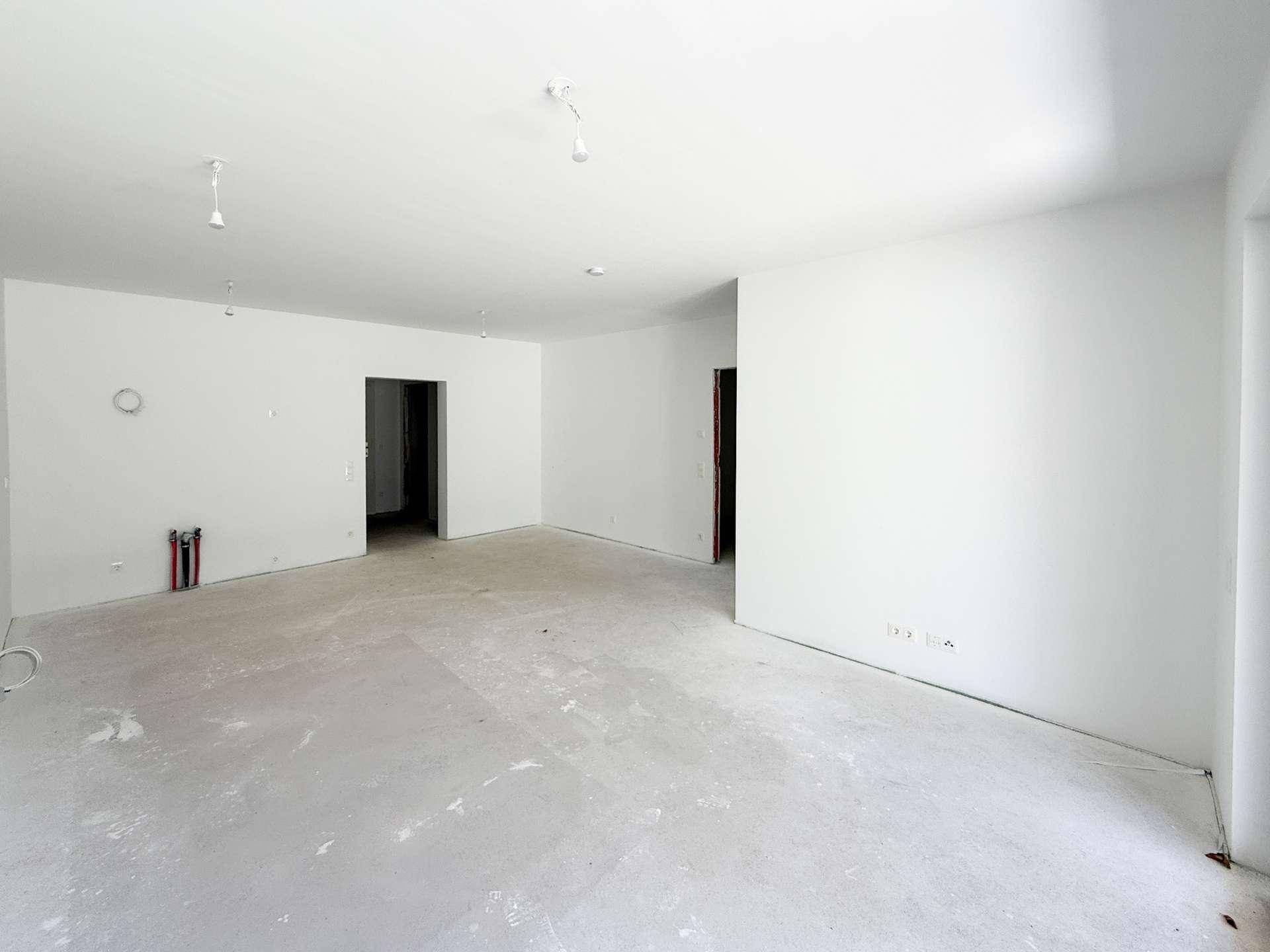 Unmöblierter Raum im Neubau mit weißen Wänden und Betonboden, bereit für den Ausbau.
