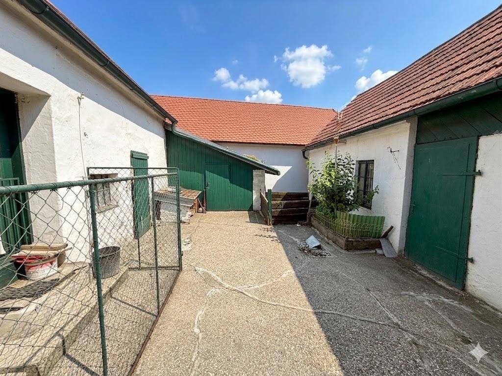 Geräumiger Innenhof mit alten Gebäuden, grünen Holztoren und einem sonnigen Ambiente.