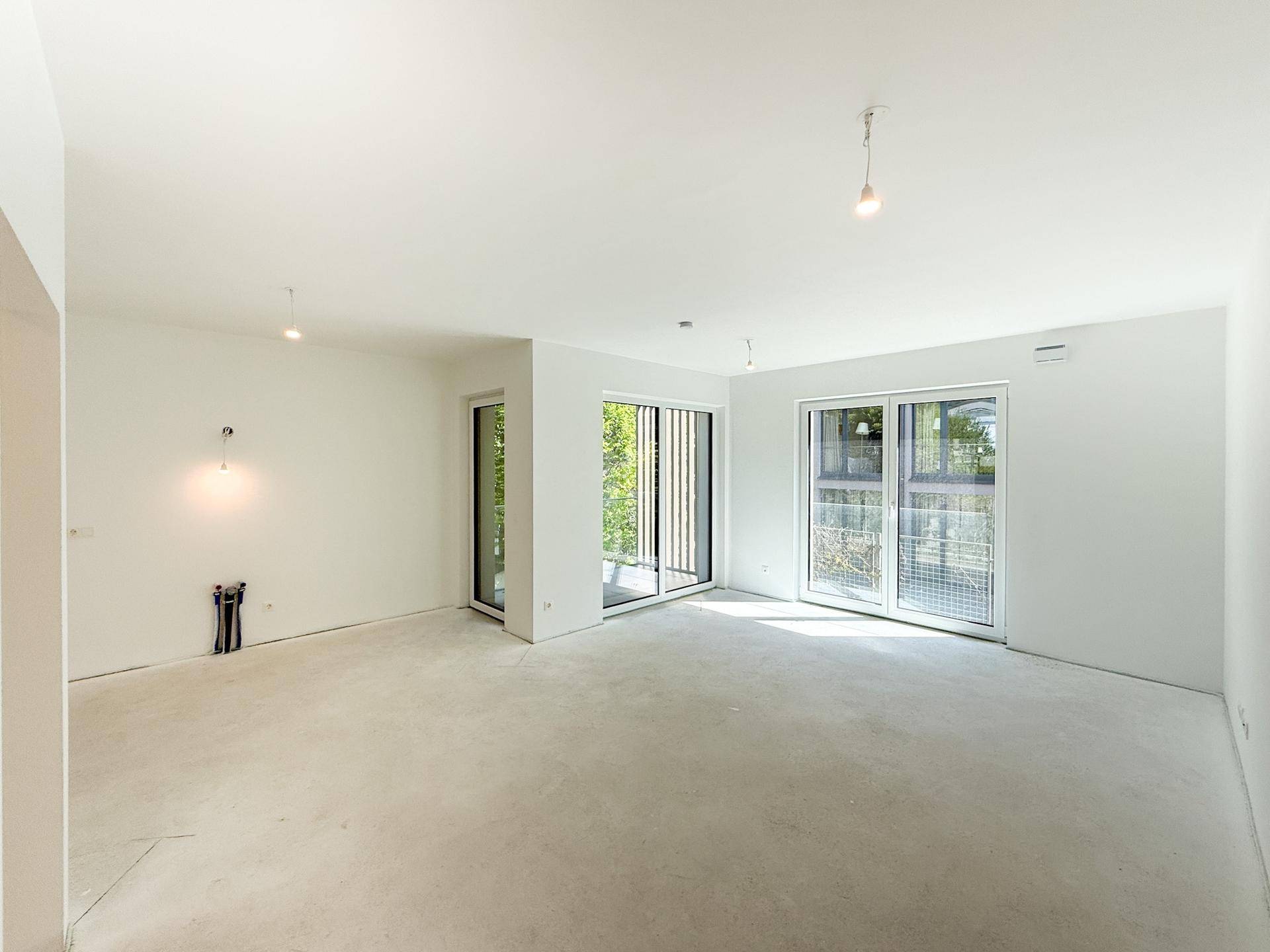 Geräumiger, unmöblierter Raum im Neubau mit viel Tageslicht und Blick auf die Umgebung.