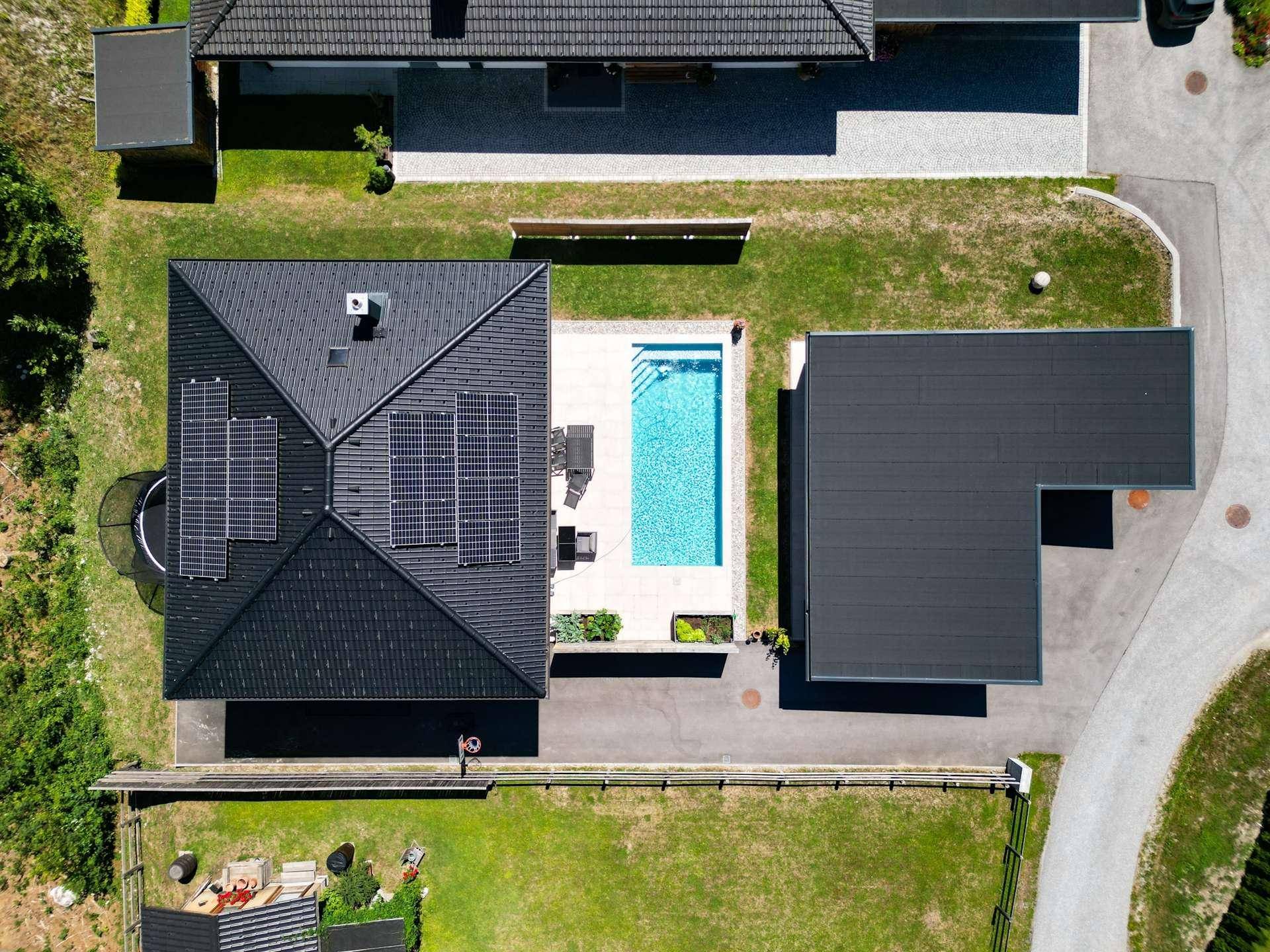 Draufsicht auf das Anwesen mit Hauptgebäude, Swimmingpool und einem L-förmigen Carport auf gepflegtem Rasen.