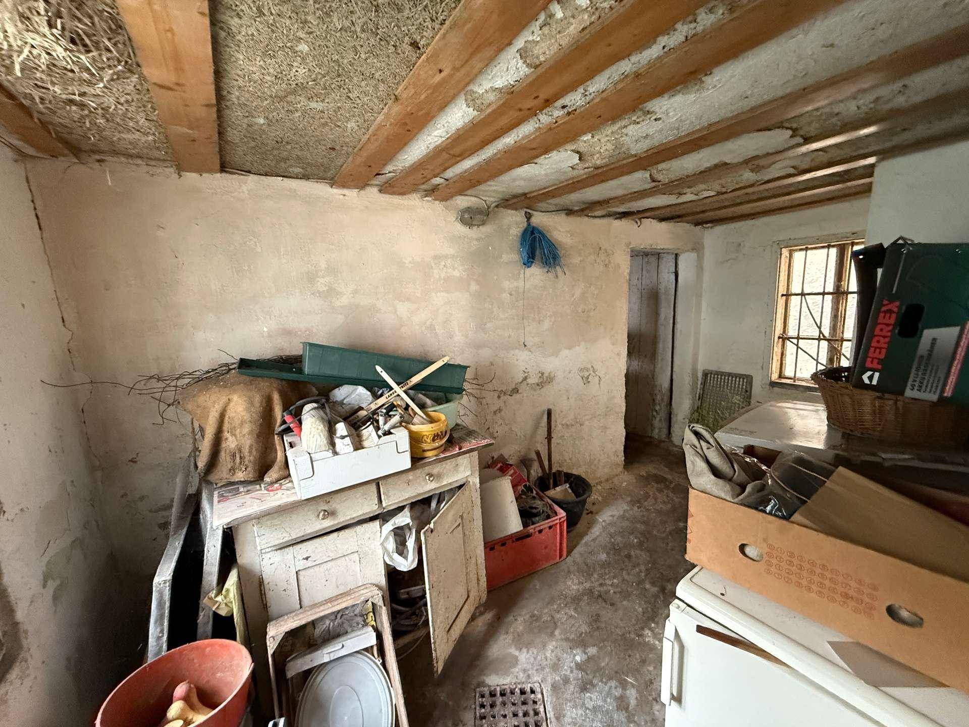 Rustikaler Raum mit sichtbaren Holzbalken und alten Möbeln, möglicherweise als Werkstatt genutzt.
