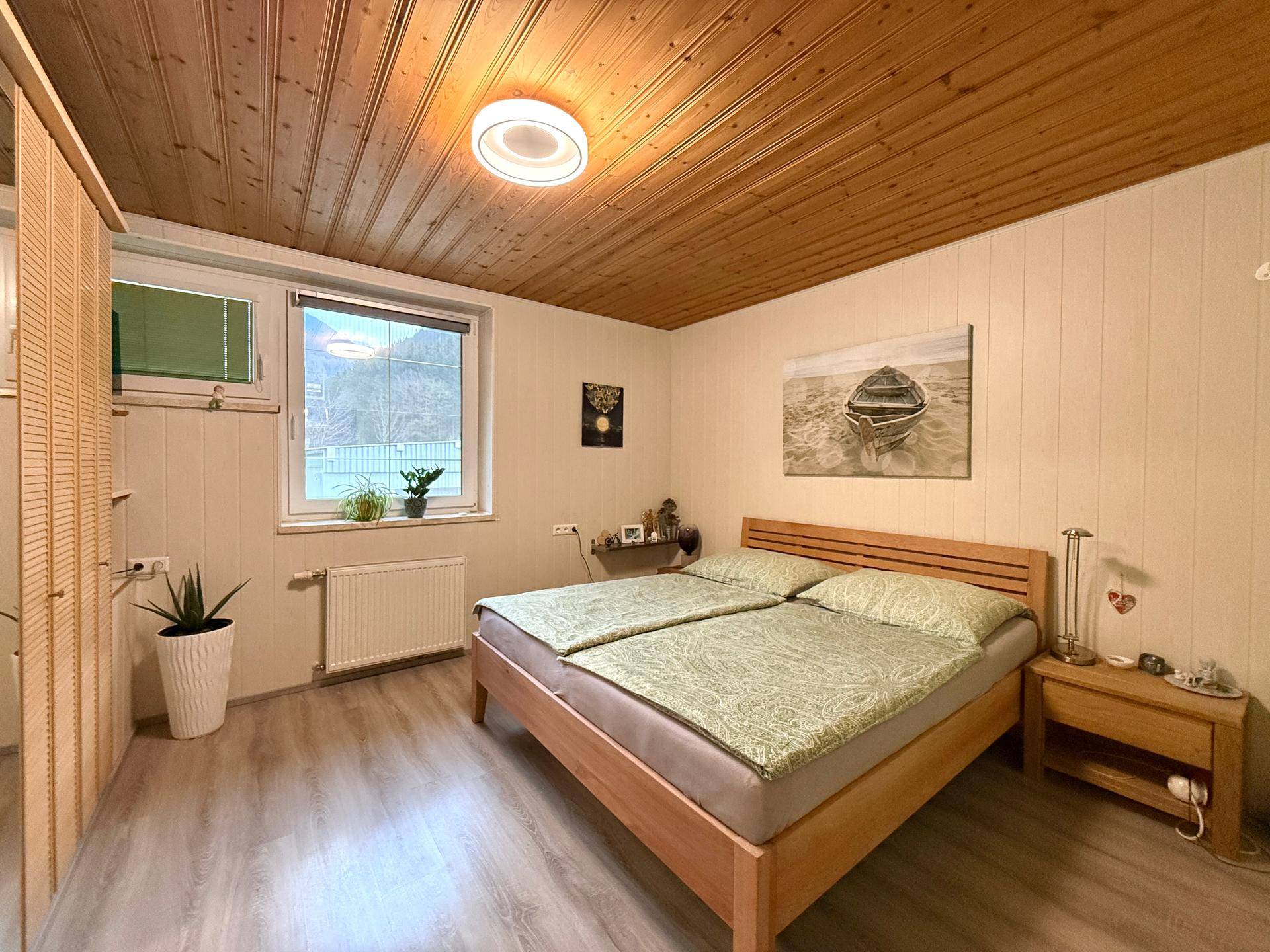 Schlafzimmer mit Holzdecke, Laminatboden und Fenster mit Blick ins Grüne.