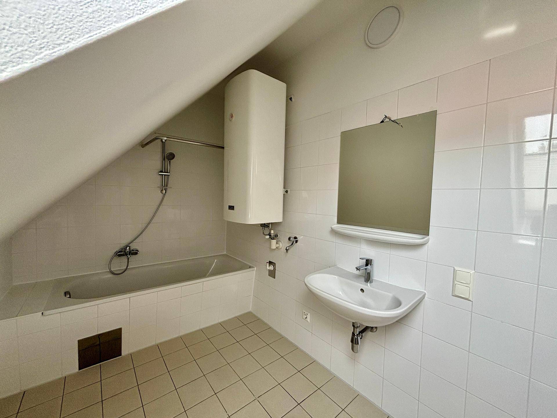 Gefliestes Badezimmer mit Badewanne, Waschbecken, Spiegel und Warmwasserboiler.