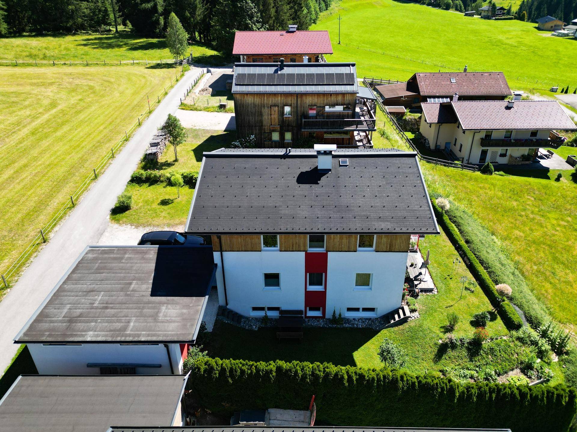 Luftaufnahme eines Hauses mit dunklem Dach, weiß-roter Fassade und gepflegtem Gartenbereich.